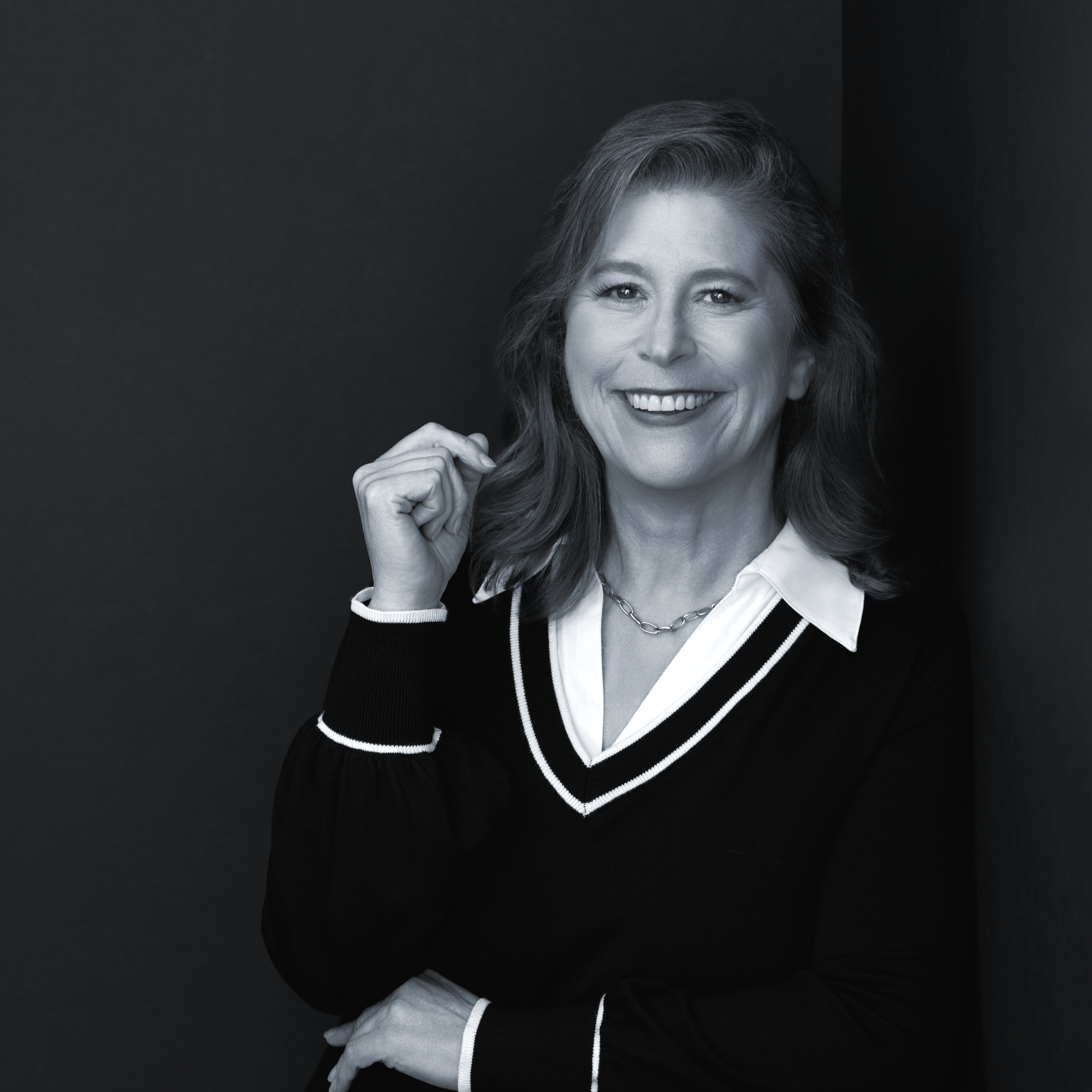 A woman wearing glasses and a sleeveless top, standing outdoors near a wooden wall with trees in the background.