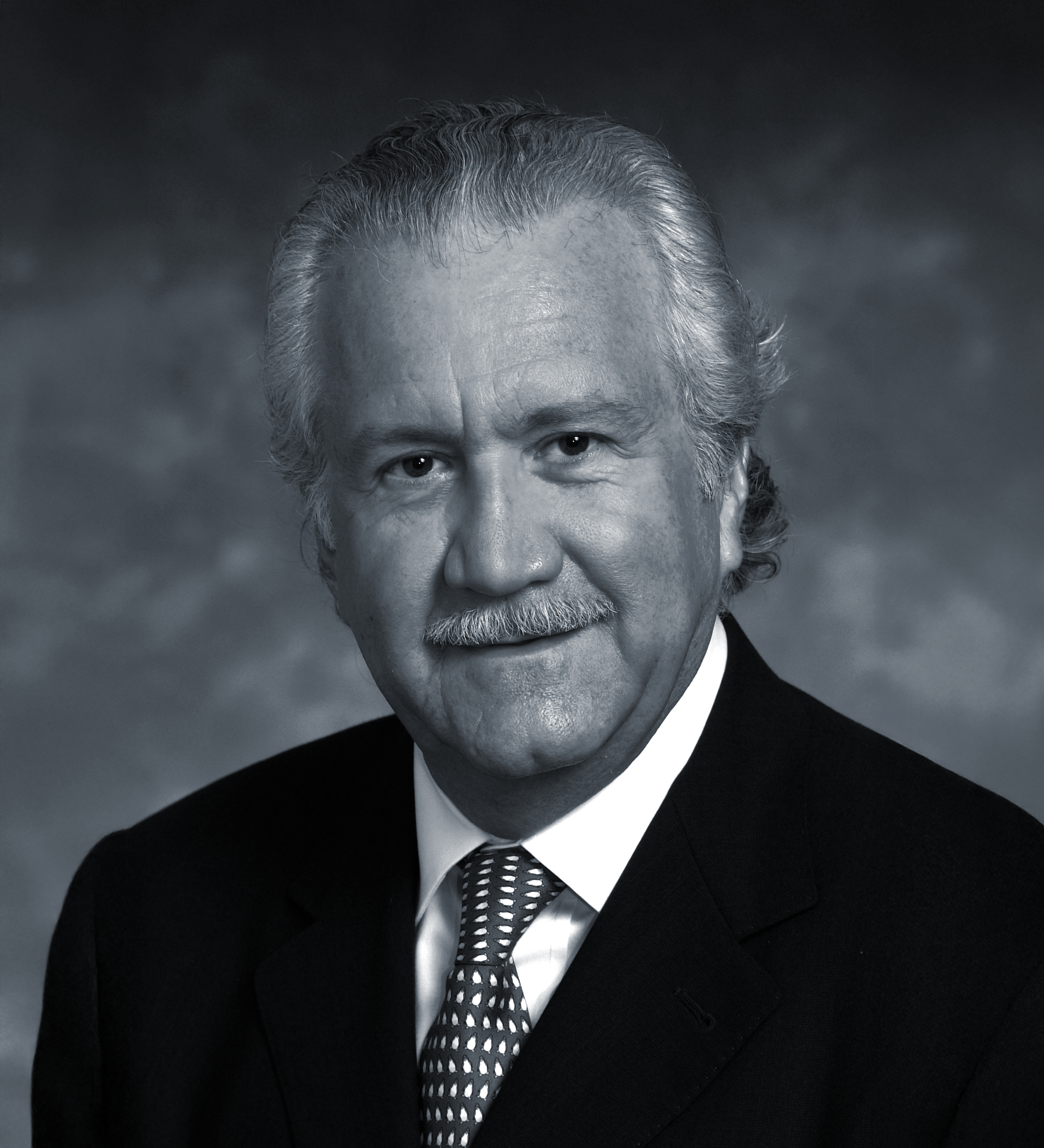 Black and white portrait of an older man with a mustache, wearing a suit and tie, smiling.