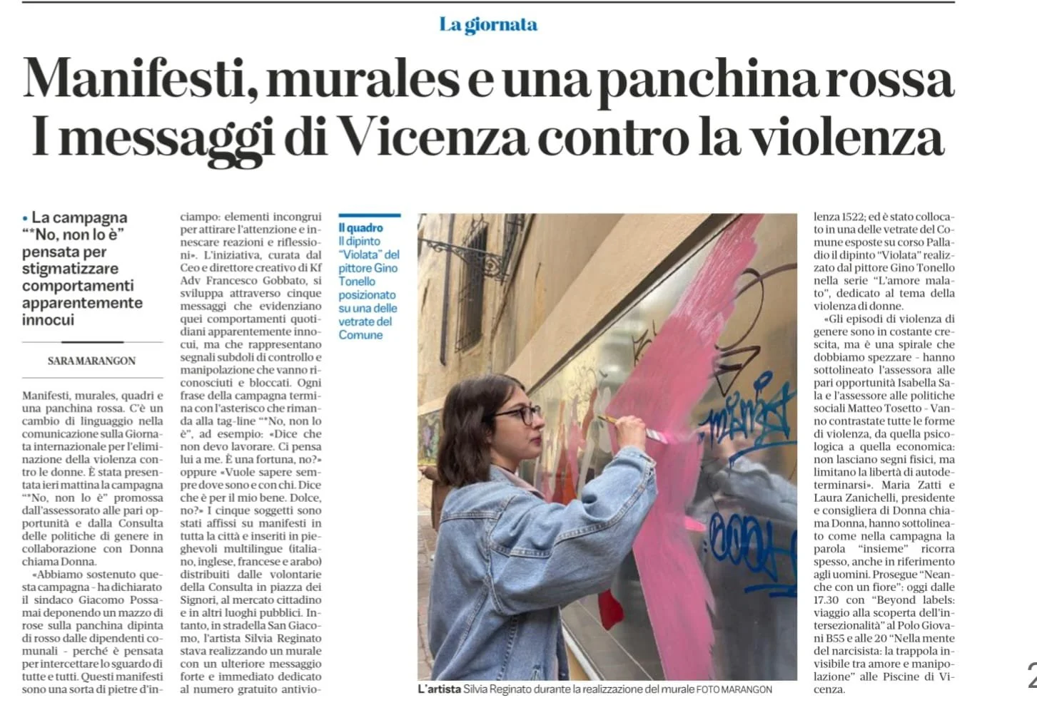 Una donna che dipinge un murale con vernice rosa su un vetro, con graffiti blu e nero. Indossa occhiali e una giacca di jeans, lavora con un pennello.