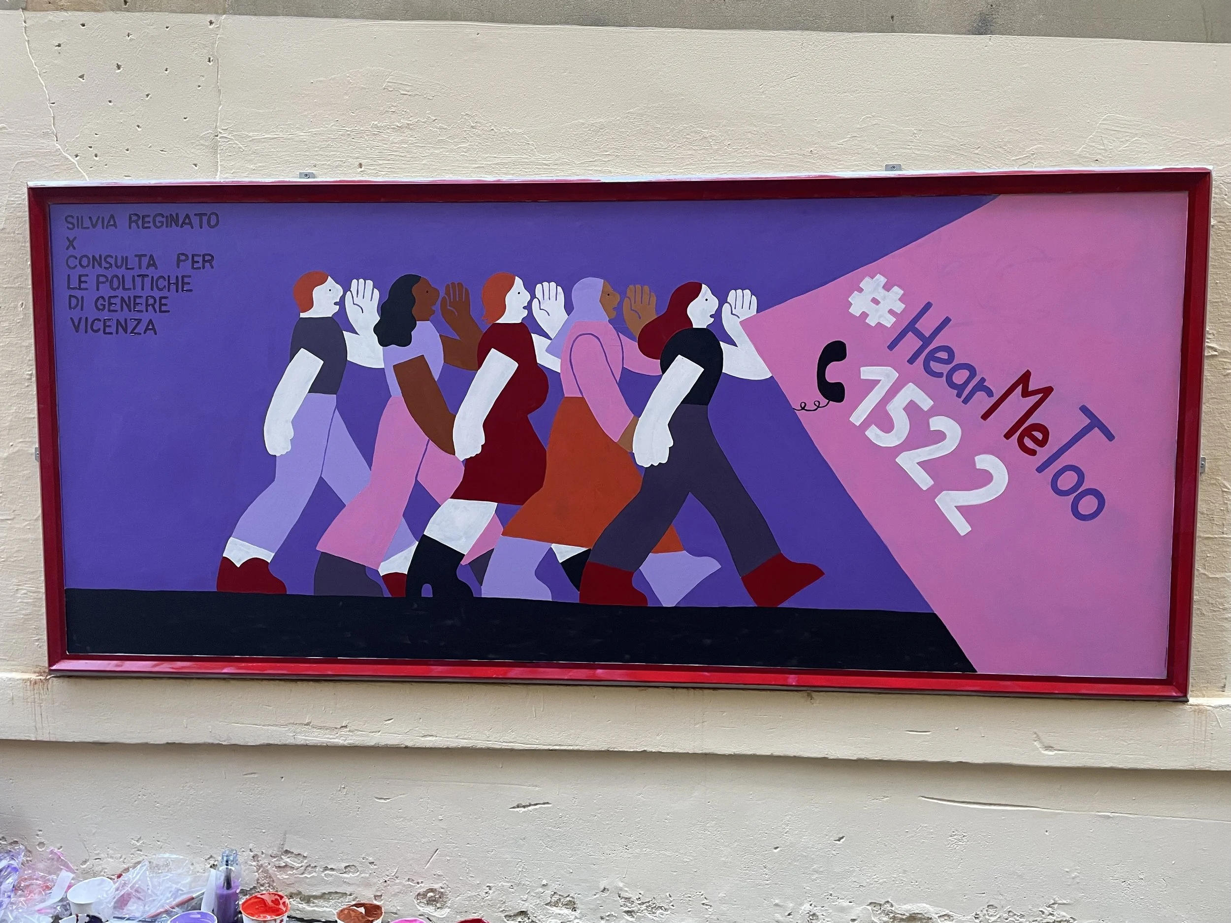 Poster con figure di donne in marcia, alcune con la bocca aperta e un telefono viola in mano, con testo che indica 'Heart Me Too' e il numero '1522', su sfondo viola e rosa.