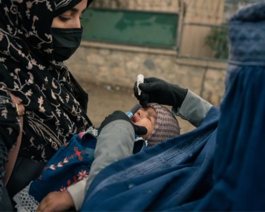 A health worker gives a polio vaccine to a child in her mother’s arms, part of a family of returnees forced out of Pakistan. ( Elise Blanchard for The Washington Post)