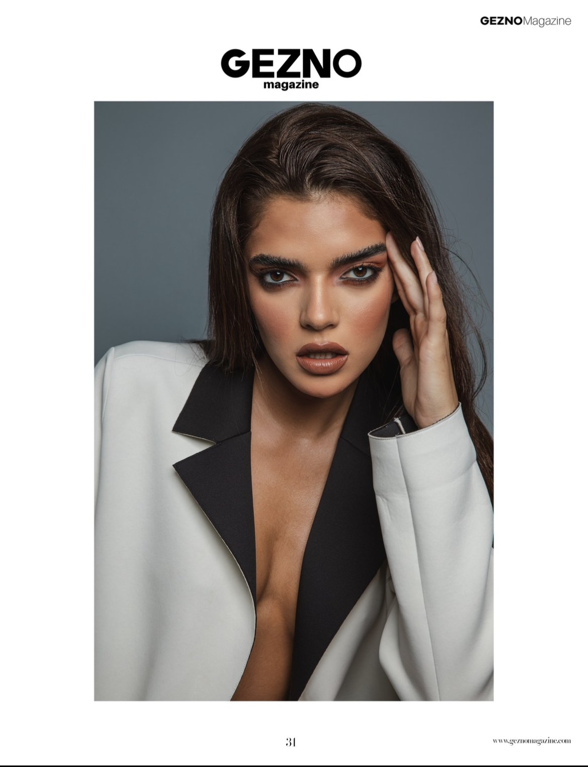 Model posing for Geznomagazine in a white and black blazer, with a hand touching her face, on the cover page.