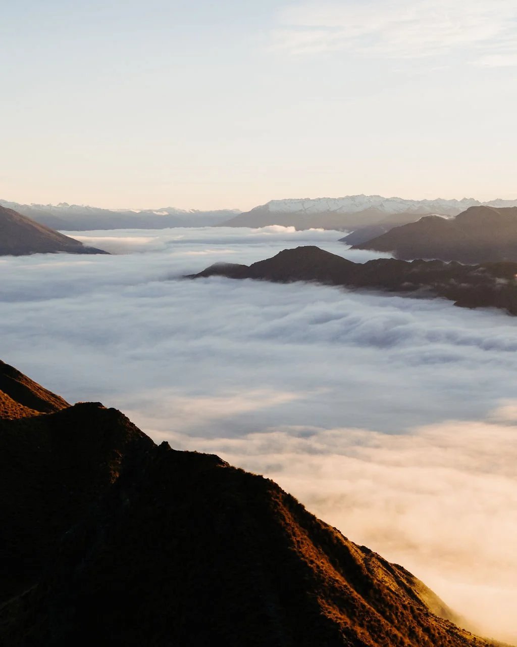 Aerial view of mountains with clouds and fog in a valley during sunrise or sunset.