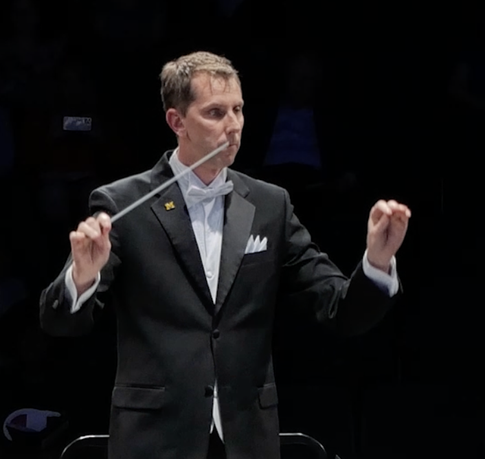 Conductor wearing a black tuxedo and white shirt directing with baton