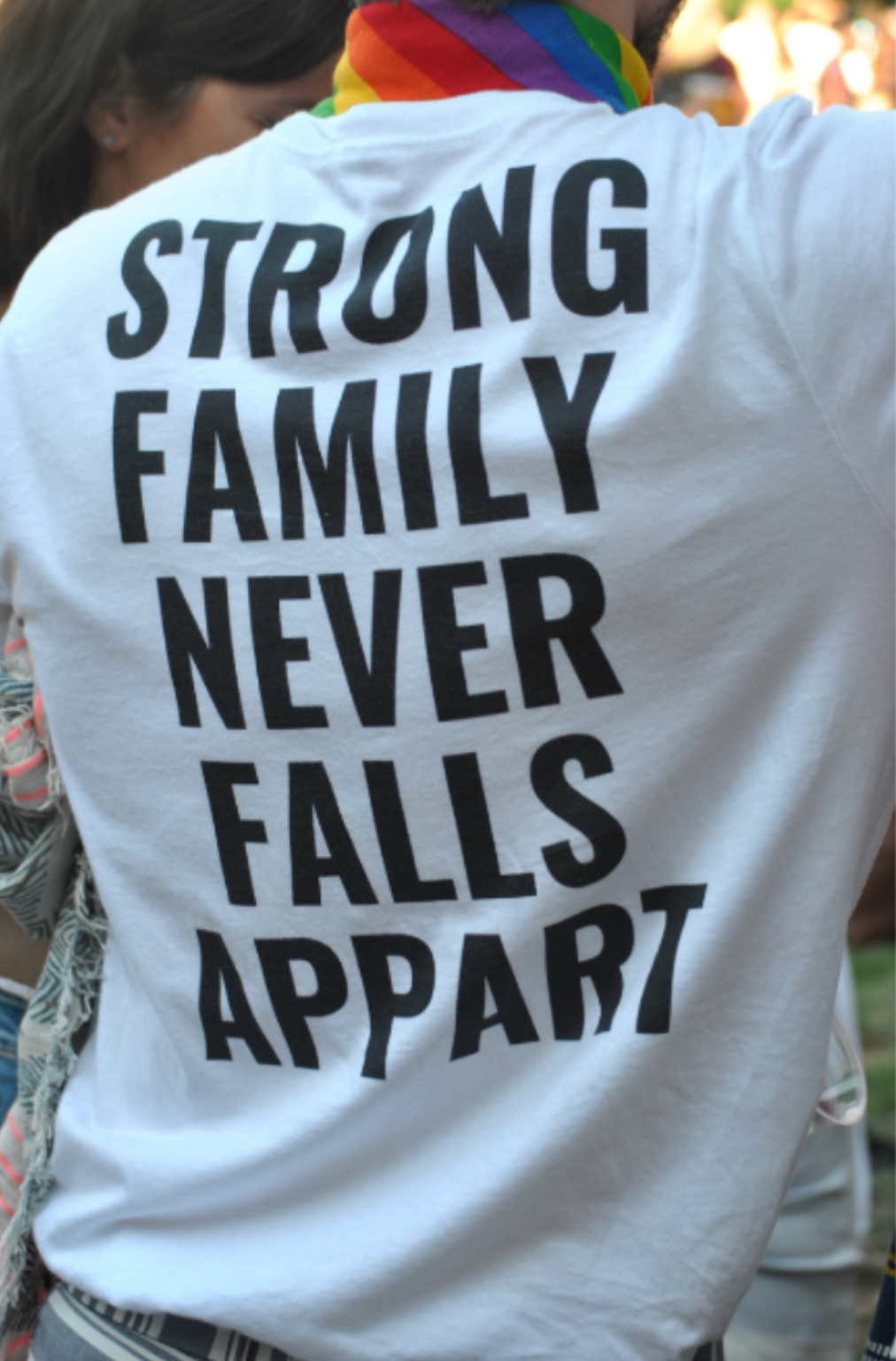 Photo of a person wearing a rainbow bandana and a white shirt that says "strong family never falls appart".
