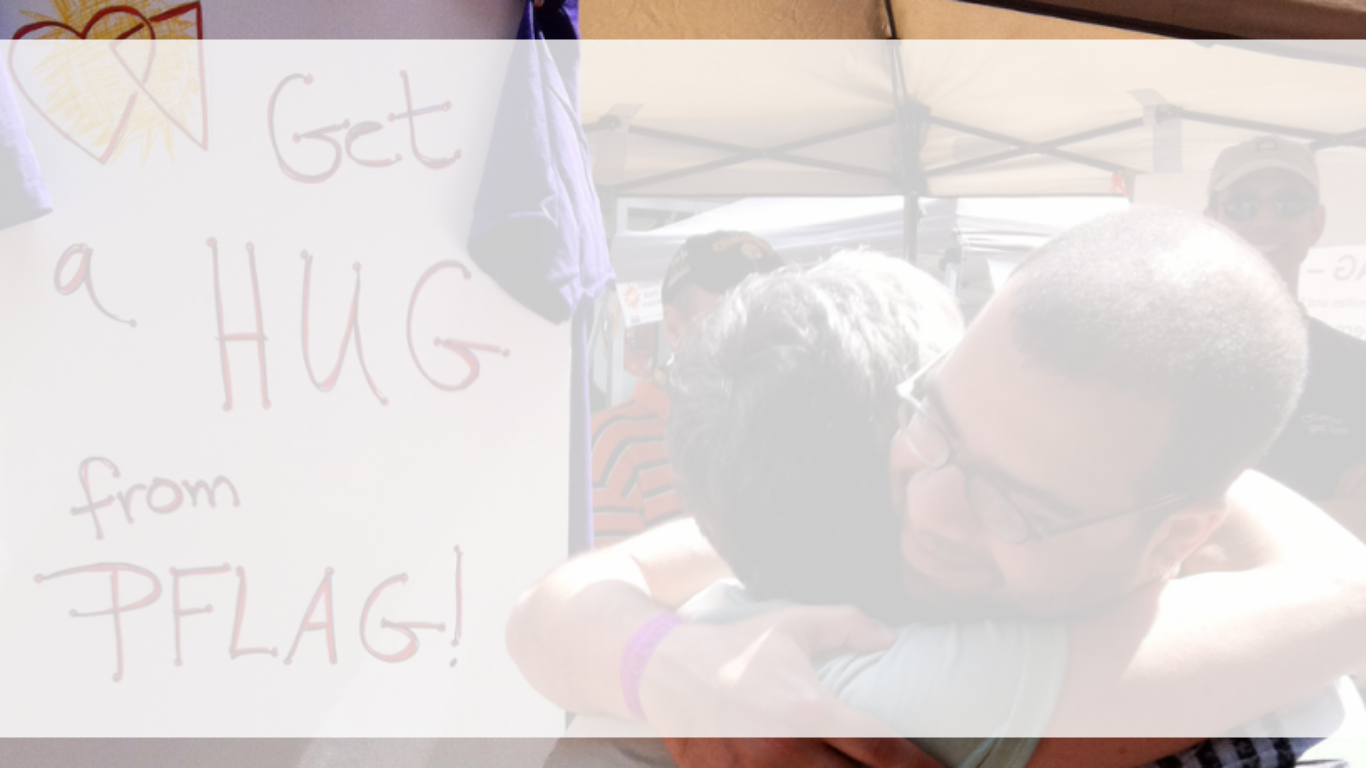 A photo. with two people hugging next to a sign with "Get a Hug from PFLAG" with a white banner overlay.