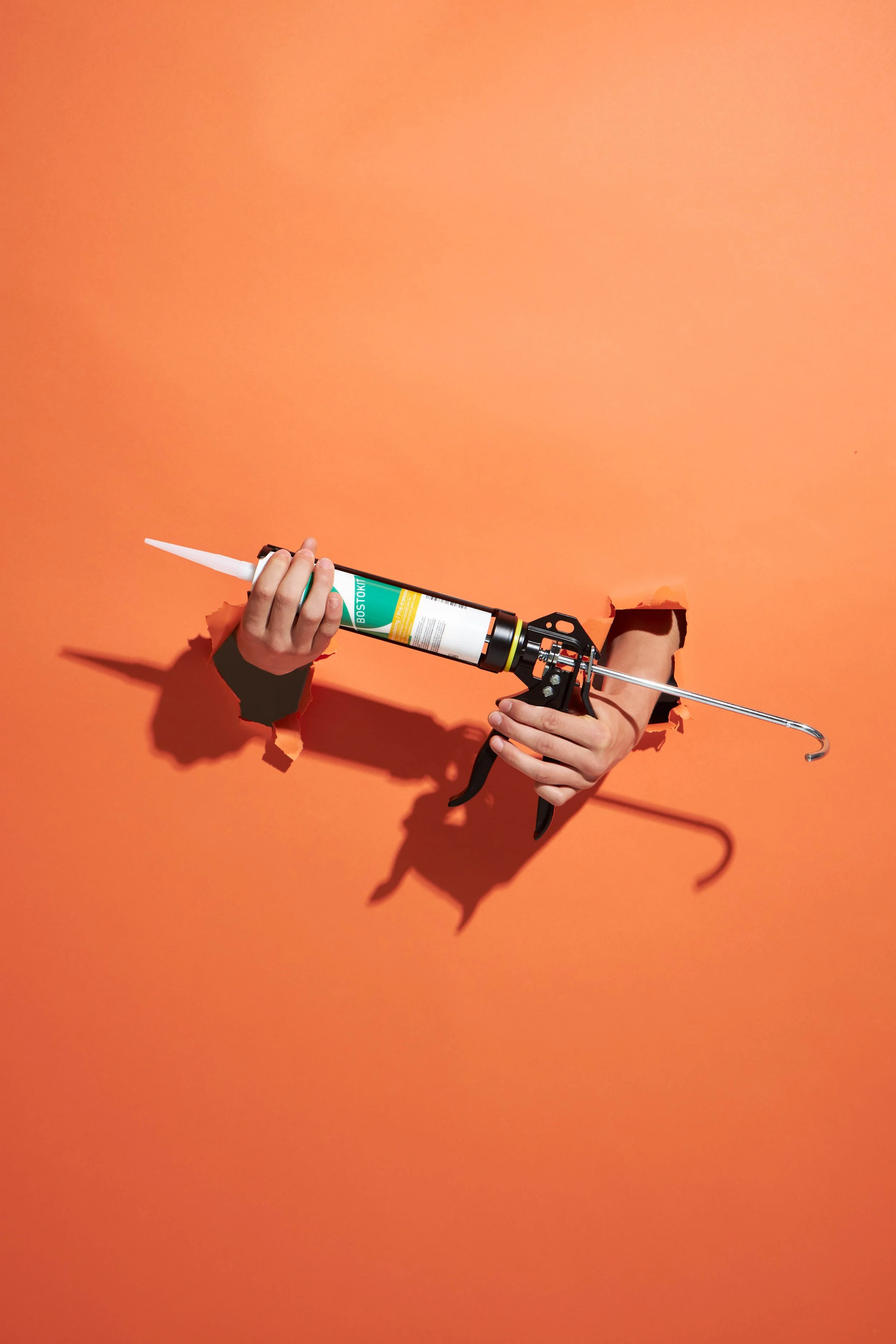 Productfoto voor BOSS Paints gemaakt in de studio van 2 handen die door de papieren achtergrond komen, beide handen hebben een silicone kit toestel vast van BOSS Paints, gefotografeerd door Simon van Rhee