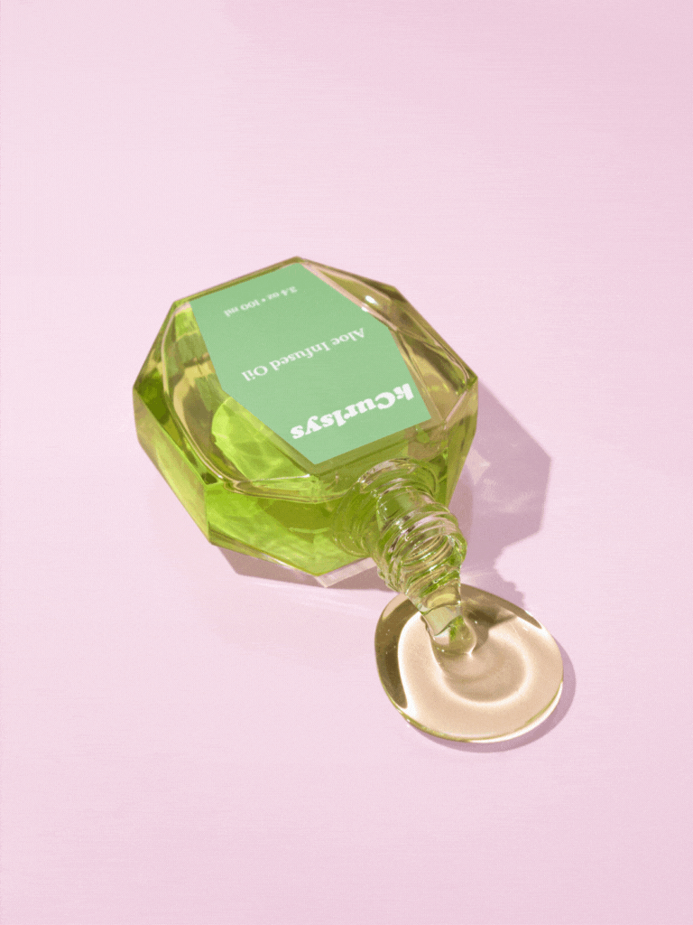 Green bottle of aloe infused oil spilling on a pink background