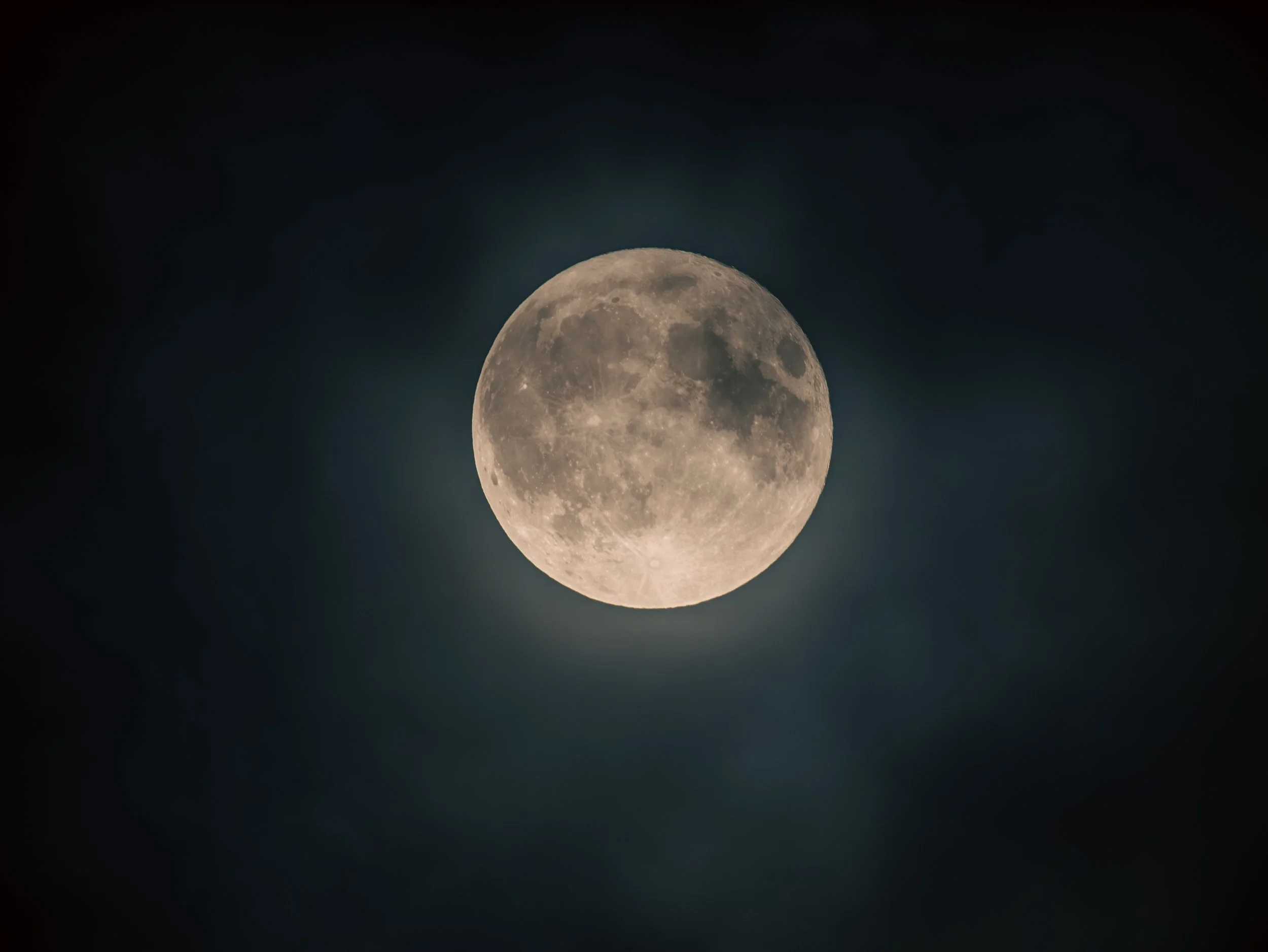 Full moon glowing in a dark night sky with some clouds surrounding it.