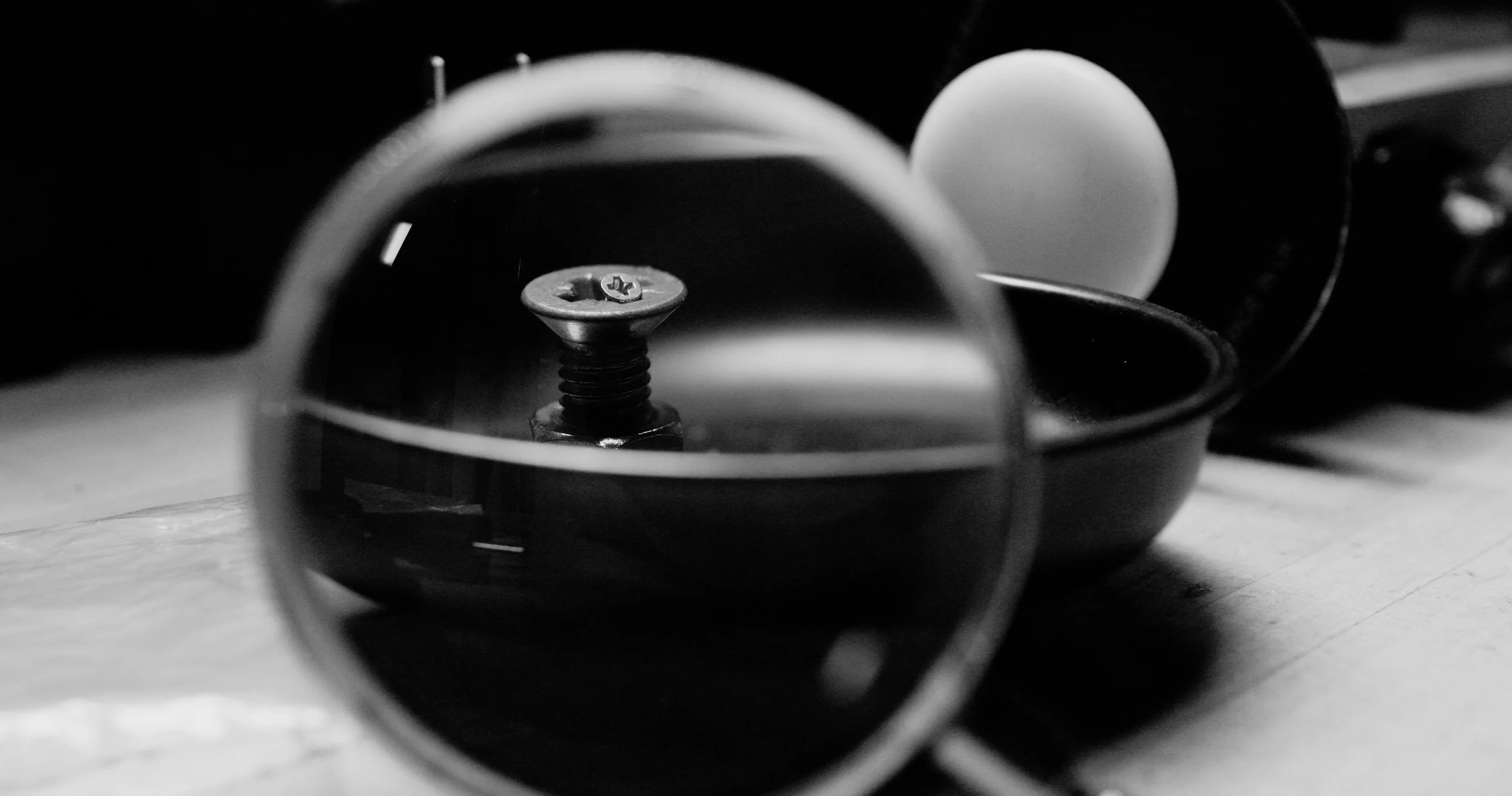 Close-up black-and-white photo of a screw in the center of a small, circular object, possibly a part of a mechanical or electronic device, with other round objects and wires in the background.