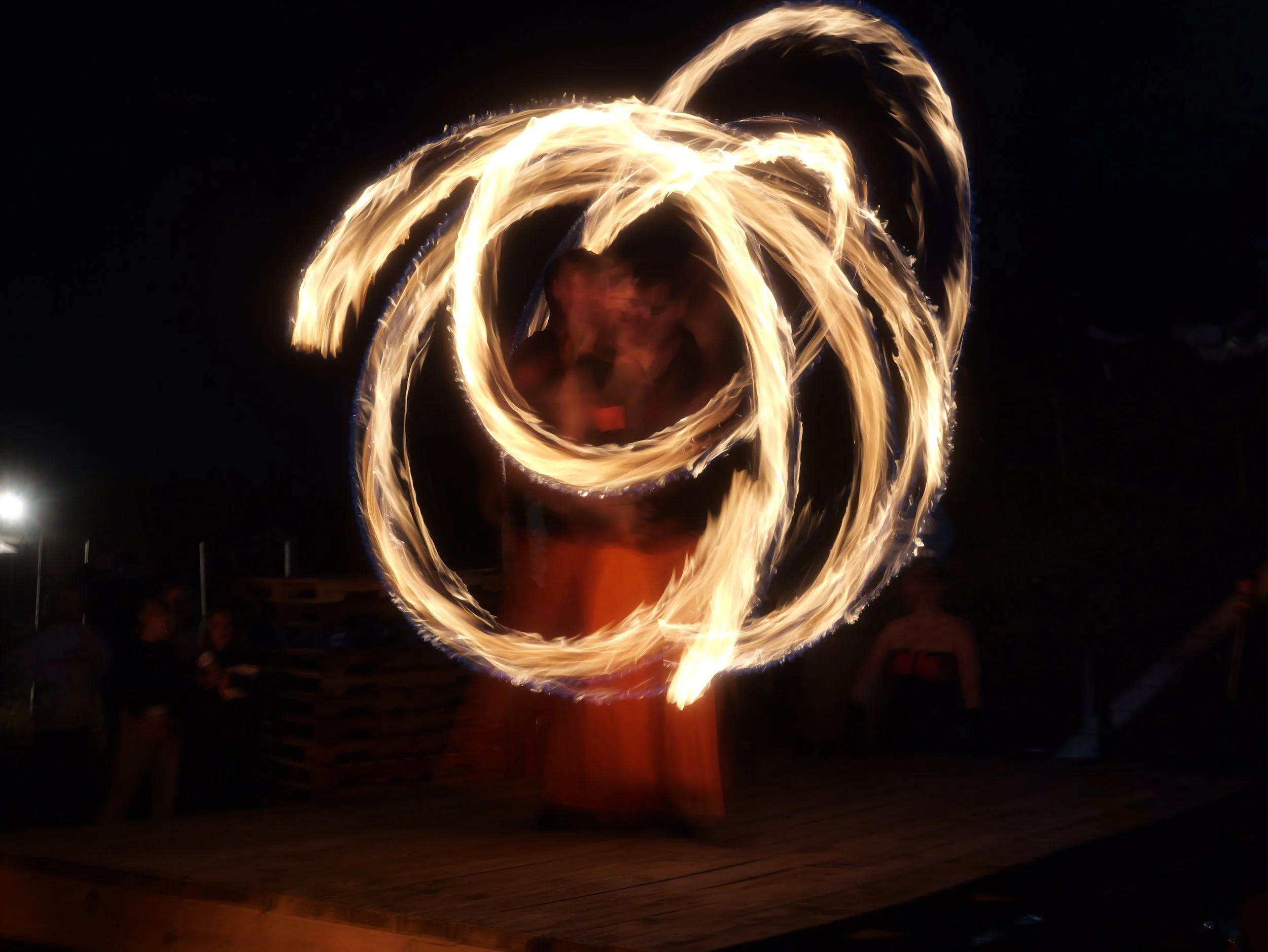 A person performing fire dancing at night, creating a spiral pattern of flames around them.
