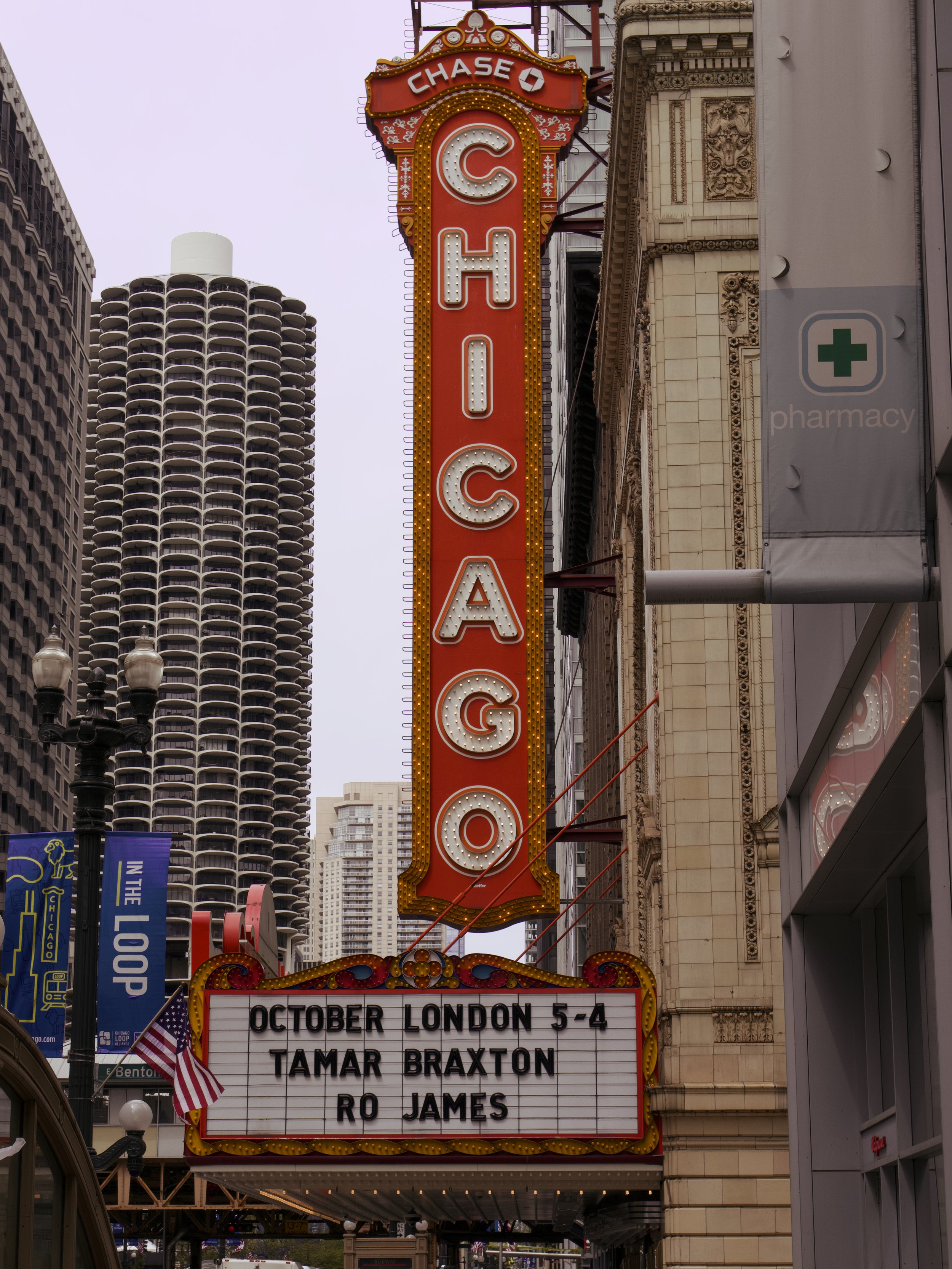 The Chicago Theatre sign in downtown Chicago, Illinois, displaying upcoming shows in October including artists like London 5, Tamar Braxton, and Ro James, with surrounding skyscrapers and banners.