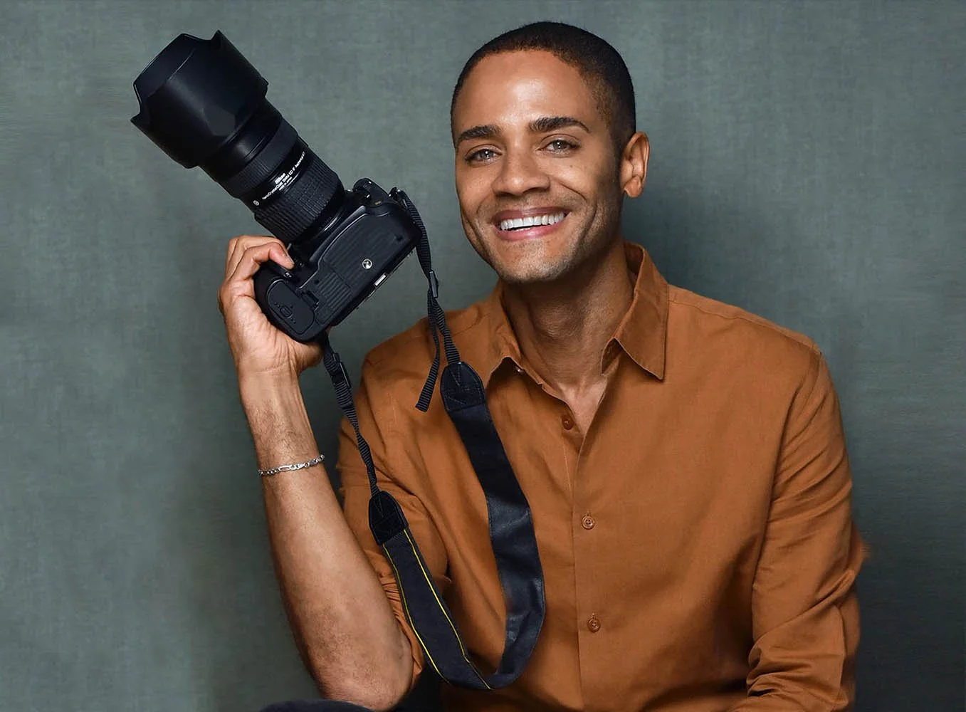 Marc Cartwright, headshot photographer, holding a camera and smiling.