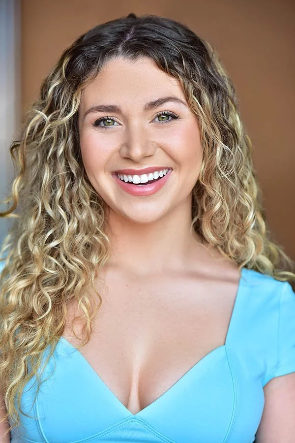 Actor in a blue top smiling against a bright, softly blurred background