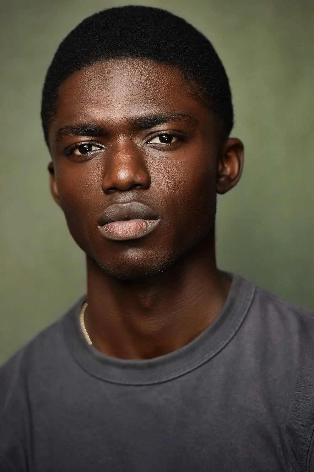 Actor headshot of a young man in a gray T-shirt with a serious expression, against a green background in Studio City, LA