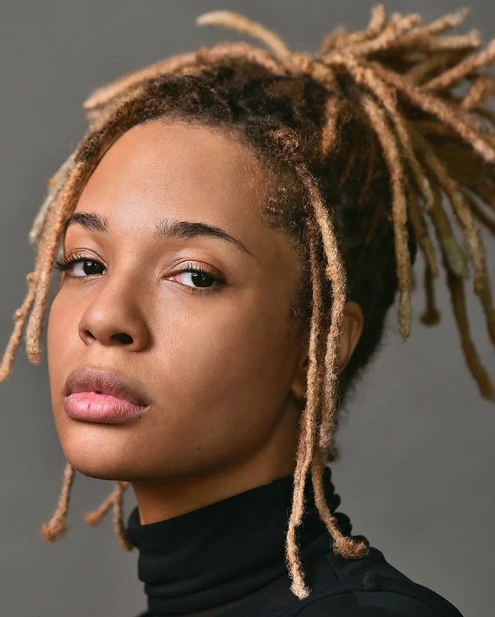 Dramatic headshot profile of a female actor with locs styled in a high bun, wearing a black mesh turtleneck with a serious expression.