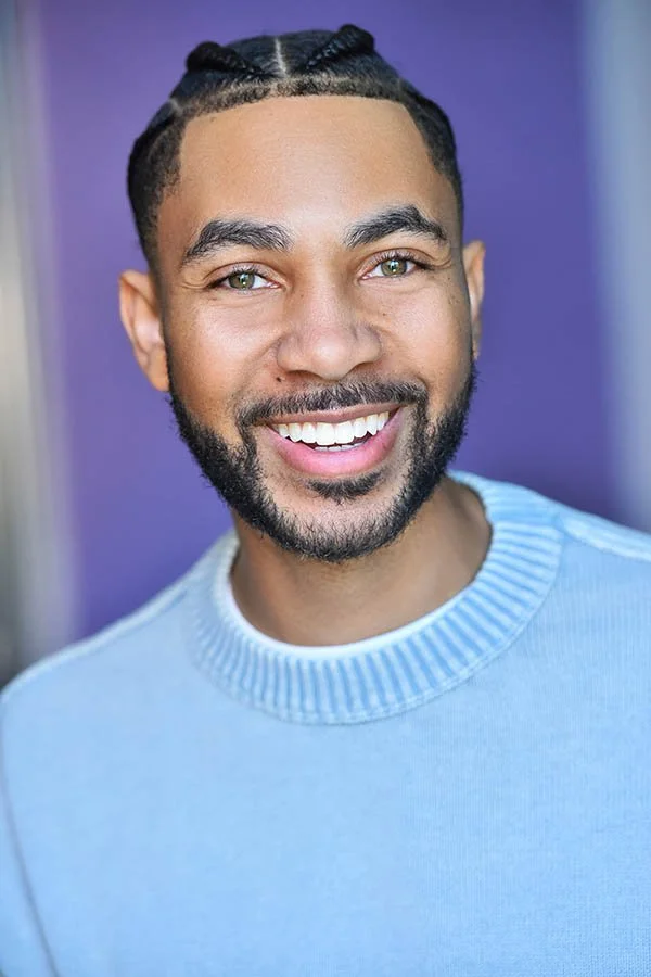 Bright commercial male actor headshot by Marc Cartwright Headshots in Los Angeles, featuring a wide smile, light blue sweater, and a purple background.