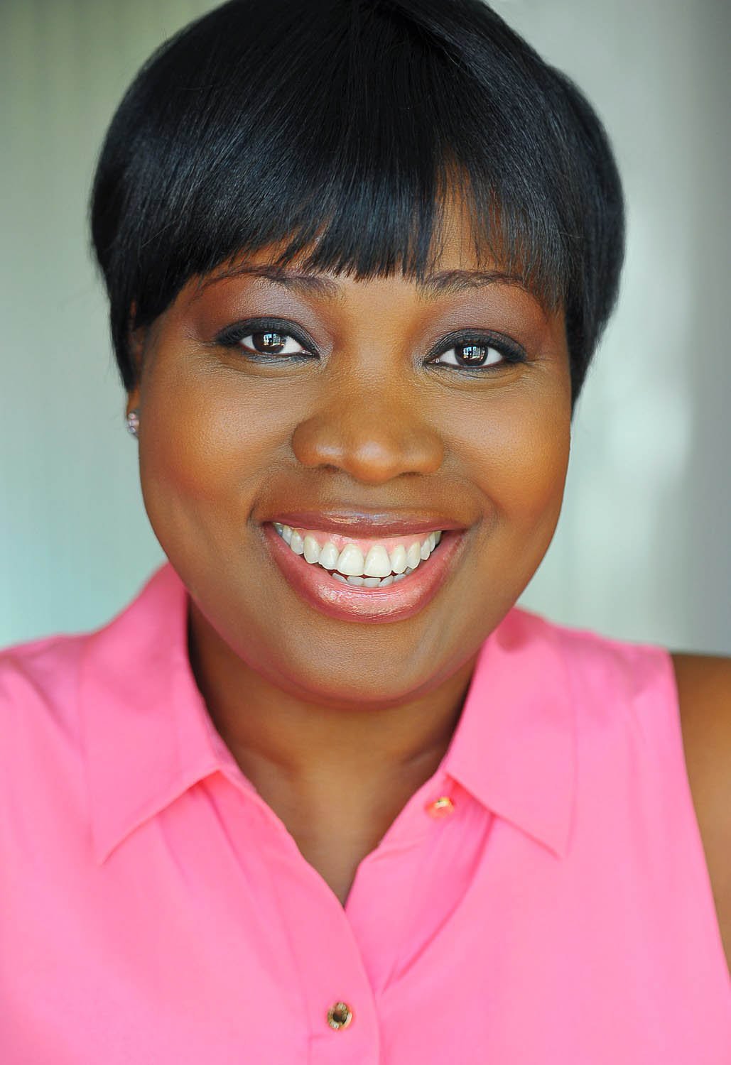 Actor headshot of a woman in a pink sleeveless blouse with a wide, bright smile