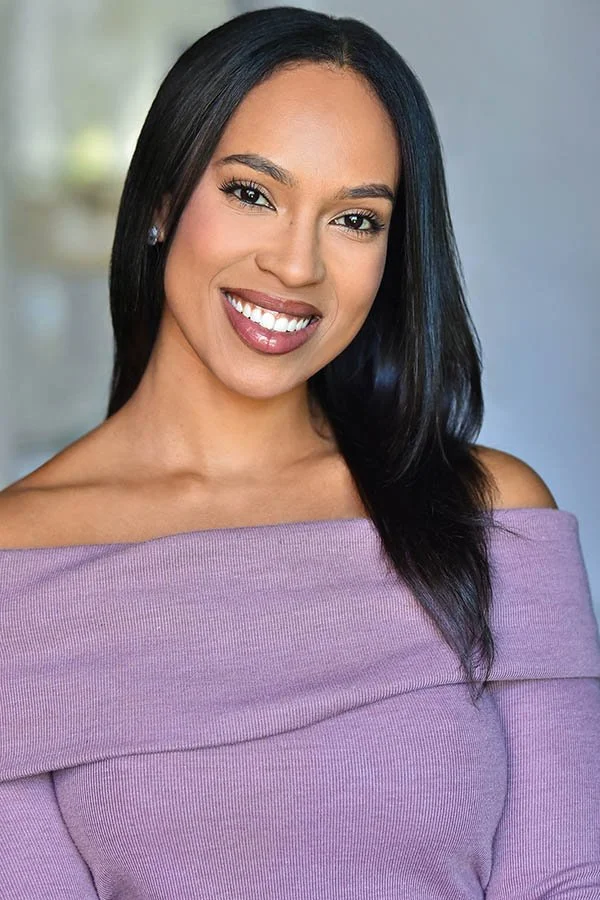 Women's commercial acting headshot featuring a smiling woman with dark hair wearing a lavender off-the-shoulder top. Studio portrait session by an LA headshot photographer.