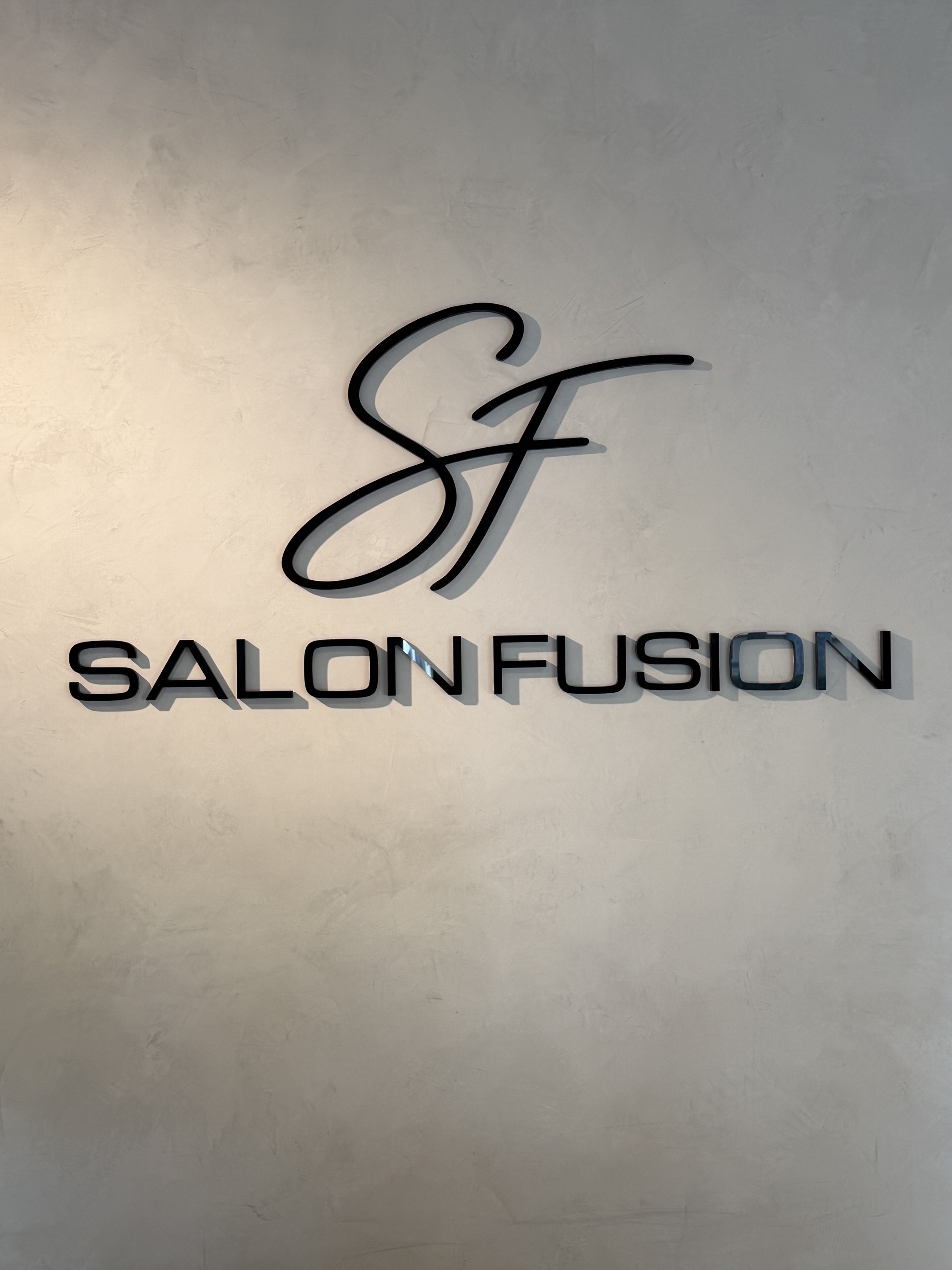 Sign with the logo of a stylized 'S' above the words 'SALON FUSION' on a textured wall.