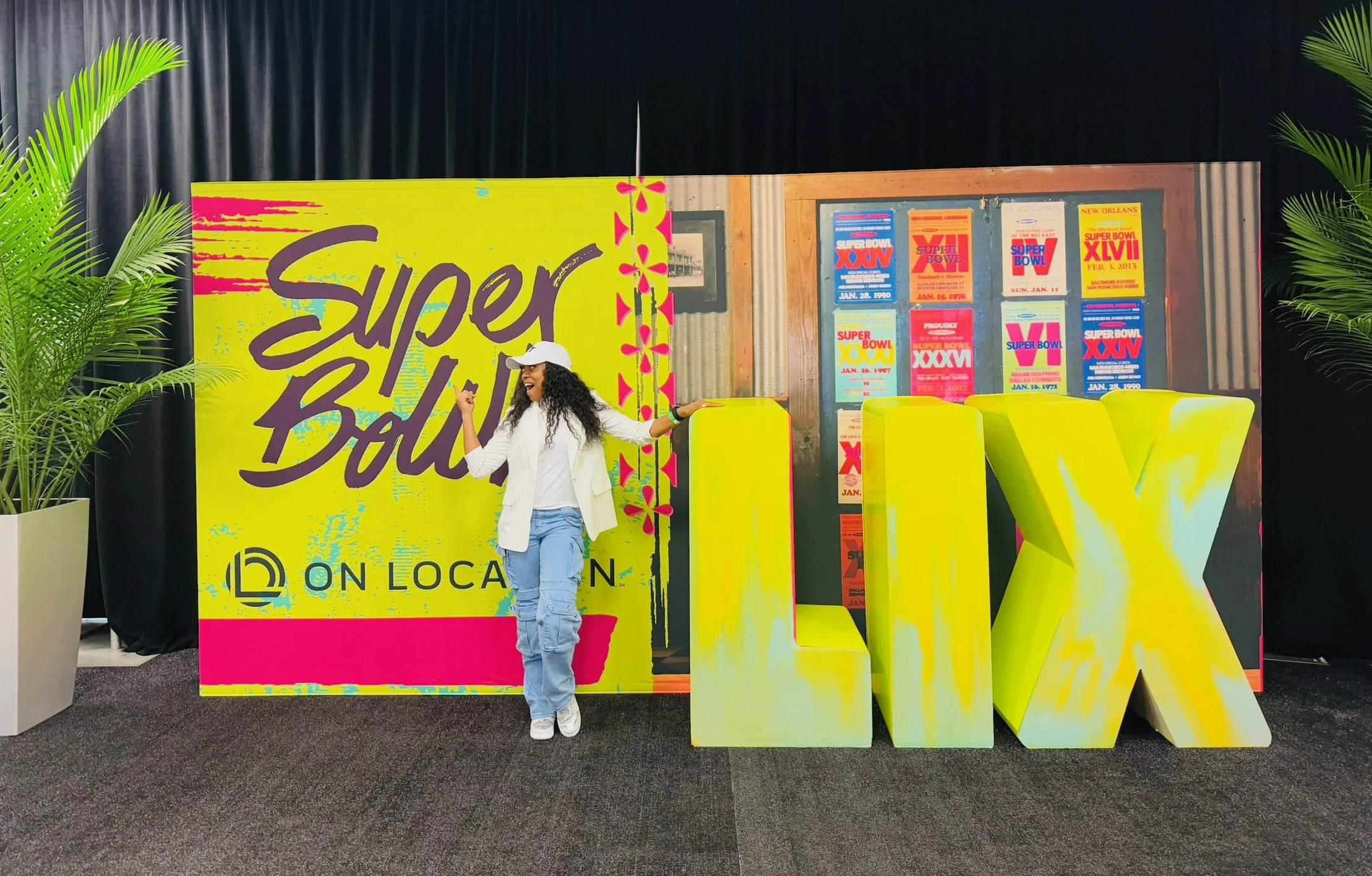 A woman standing next to colorful Super Bowl display with large yellow 'X' letters and a backdrop of Super Bowl posters.