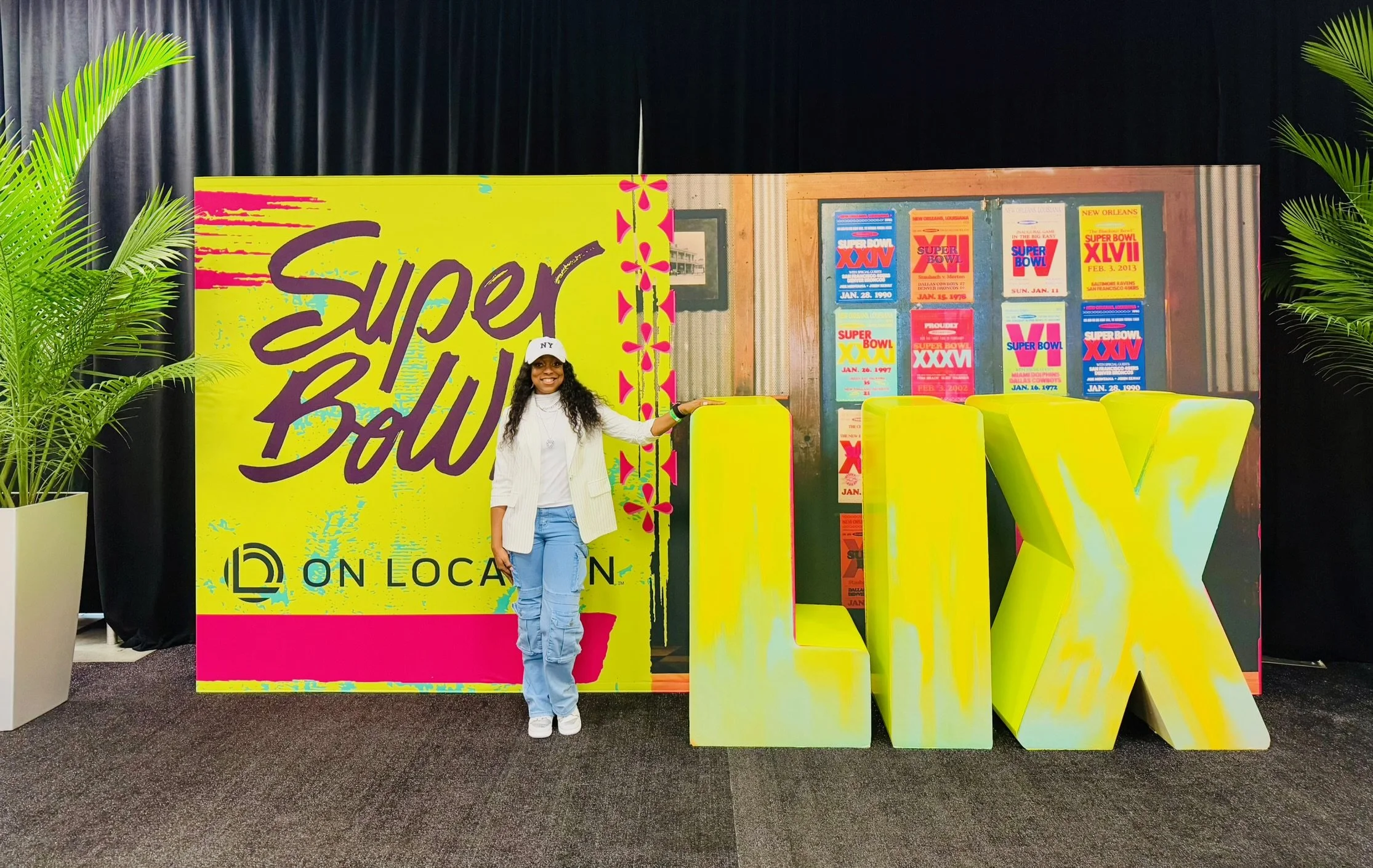 Woman standing next to a colorful display with large yellow letters "LV" and a bright background reading "Super Bowl".