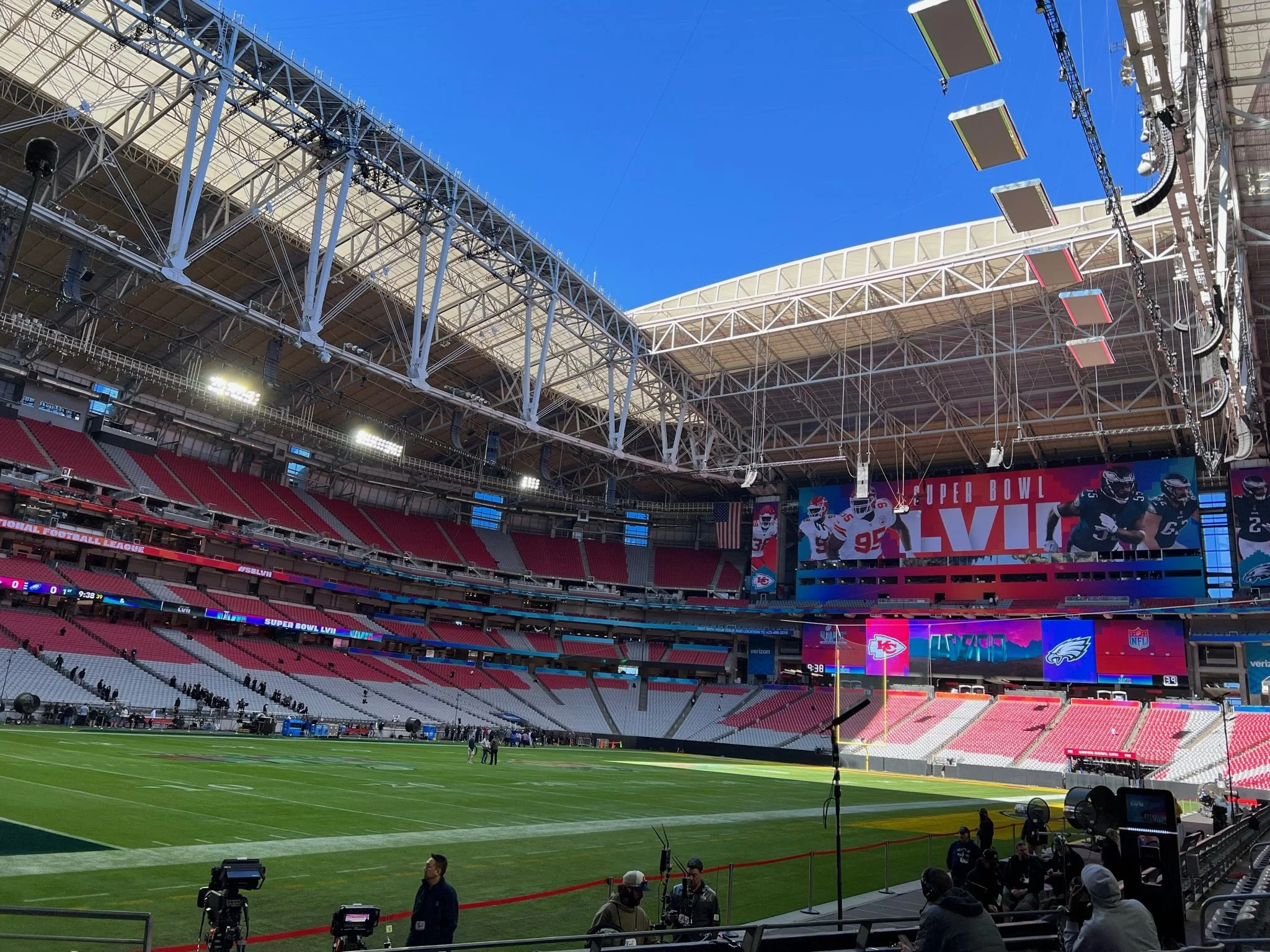 Inside a large stadium with red seating, green field, and large screens displaying football players and Super Bowl LIV branding, ready for a game.