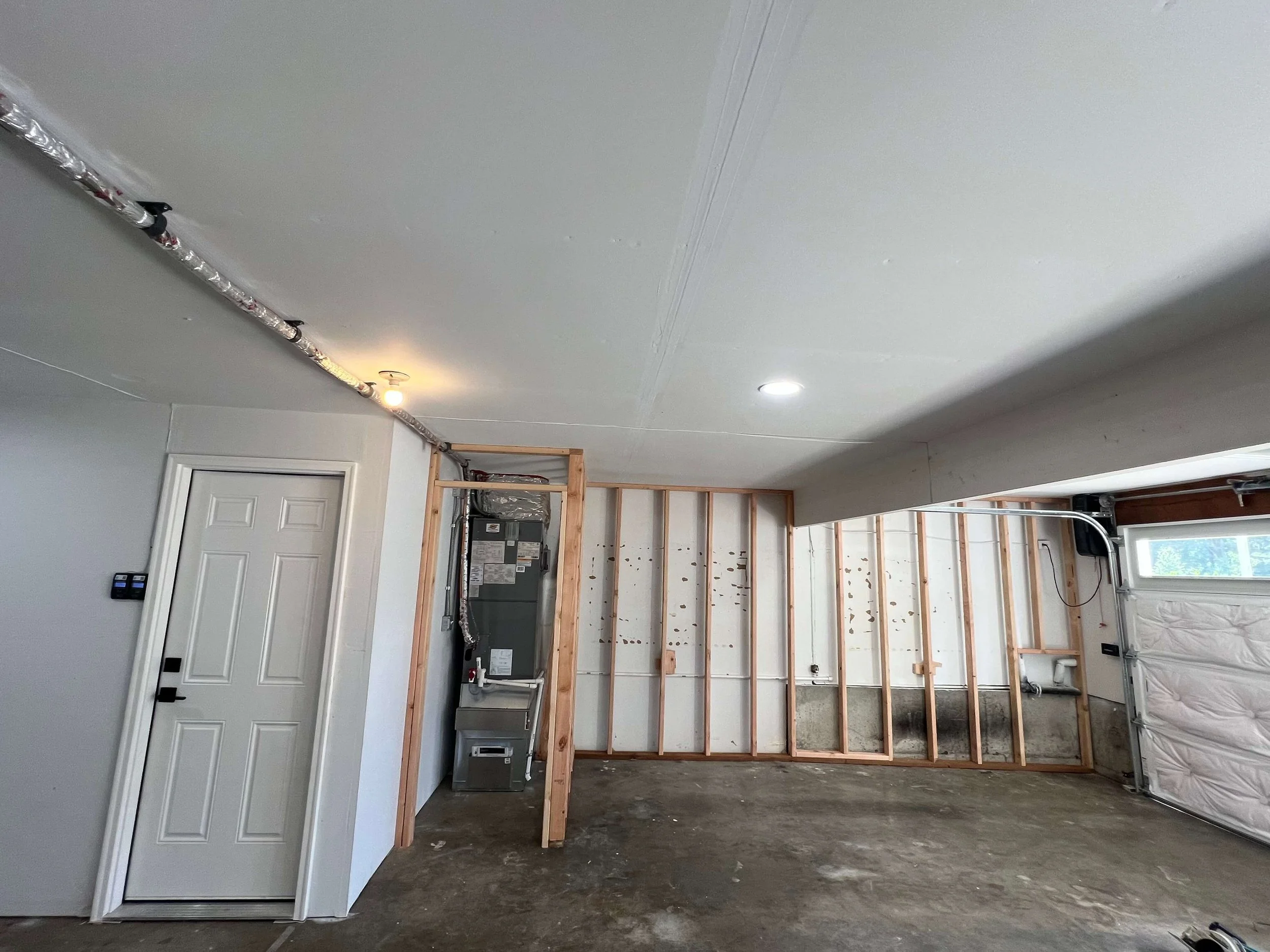 Before a Level 4 garage upgrade in Kenmore with fire-rated drywall, exposed framing, mechanical equipment, and unfinished surfaces.