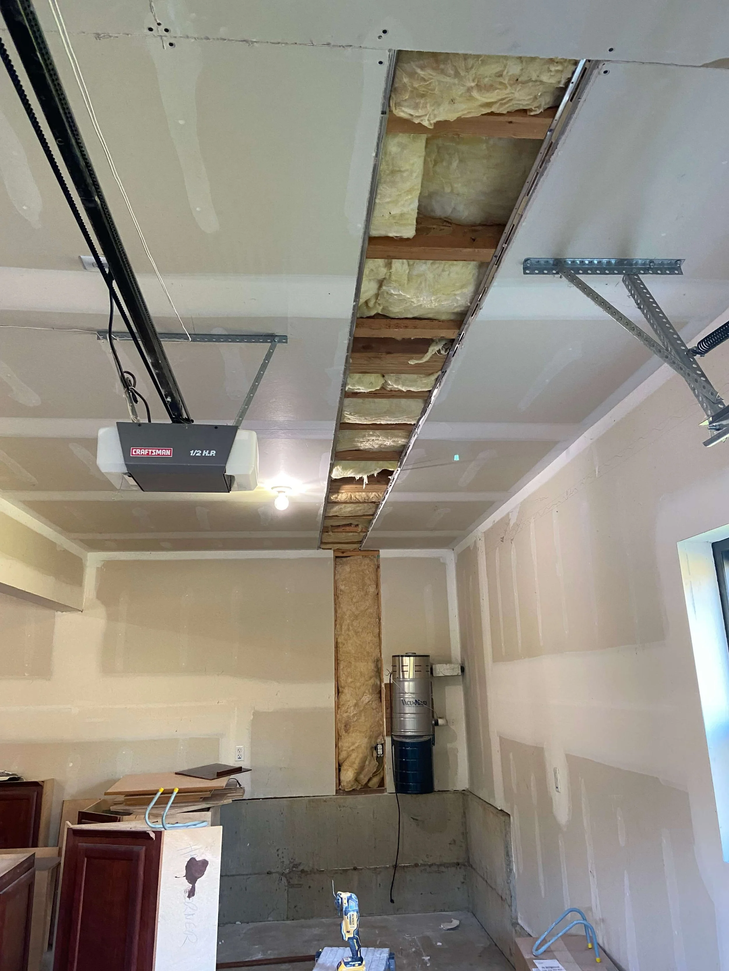 Garage with opened ceiling and wall drywall exposing framing and insulation before repair.