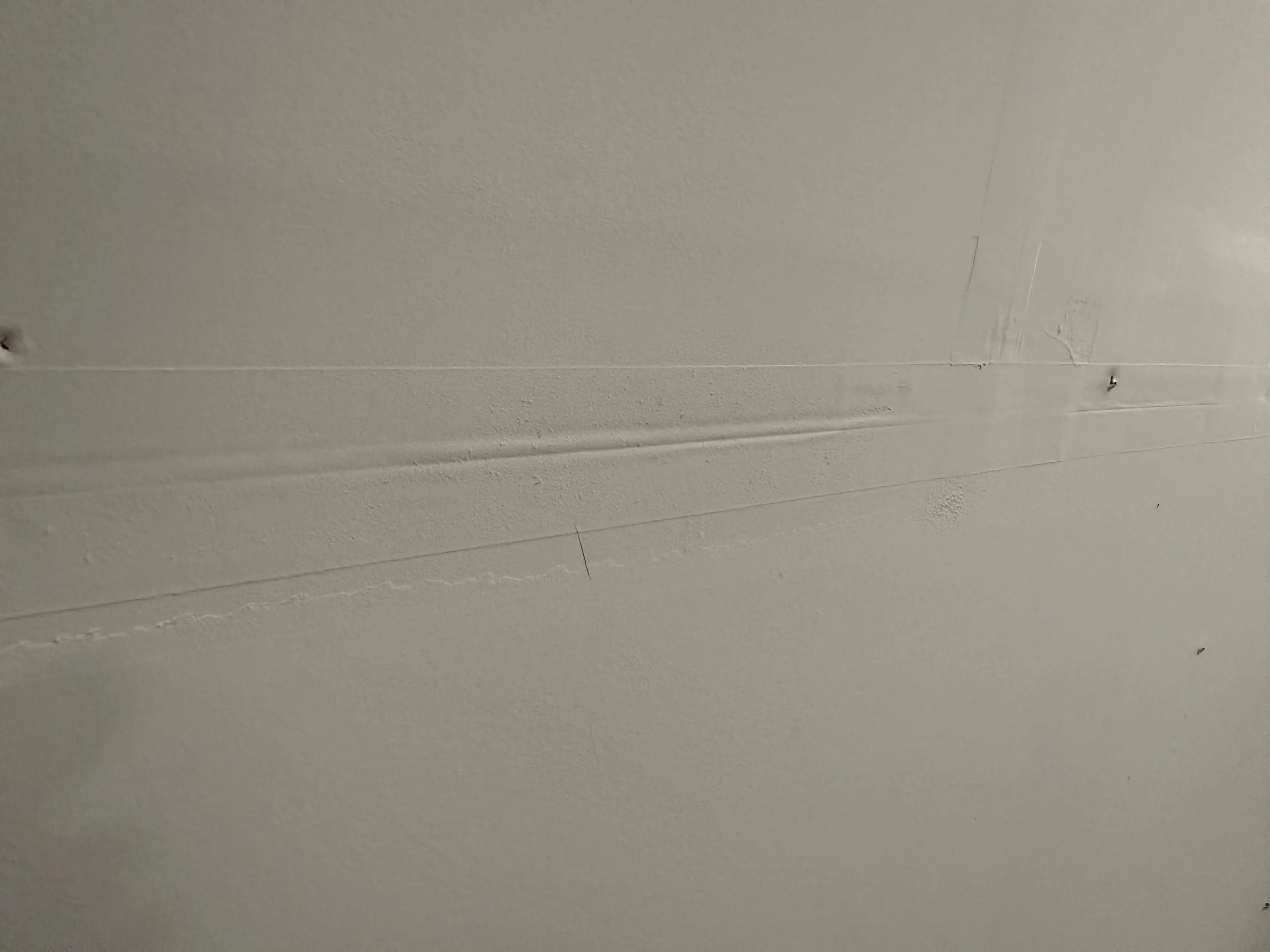 Visible drywall tape line showing through painted garage wall in Kenmore WA demonstrating common builder-grade drywall finishing imperfections
