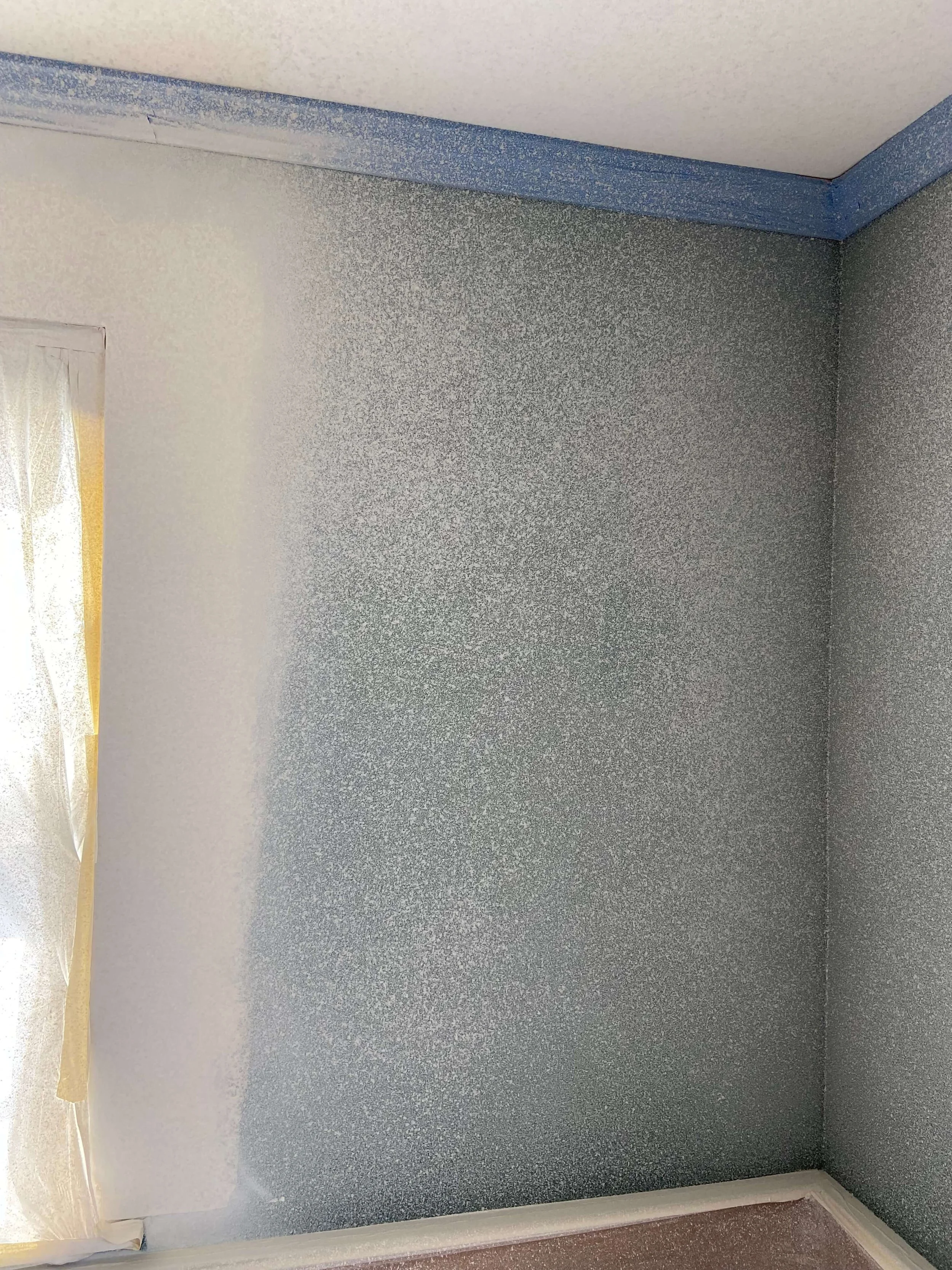 Freshly applied orange-peel texture on an interior wall beside a masked window, with trim protected during application.