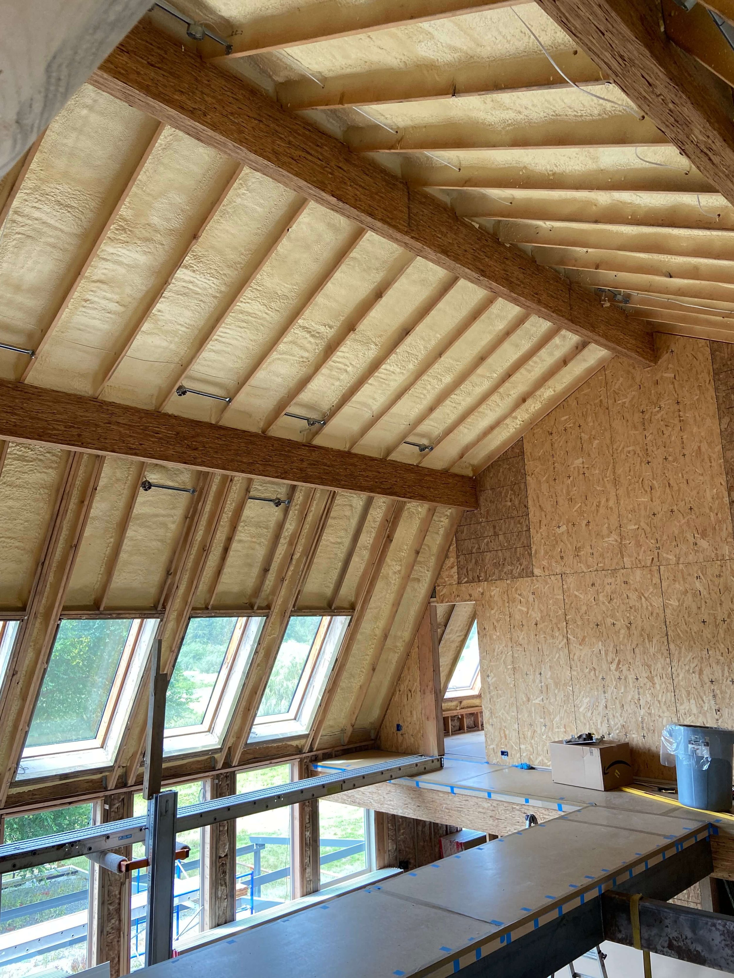 Redmond loft before drywall installation, showing exposed framing, roof insulation, wood beams, and protected walkways.