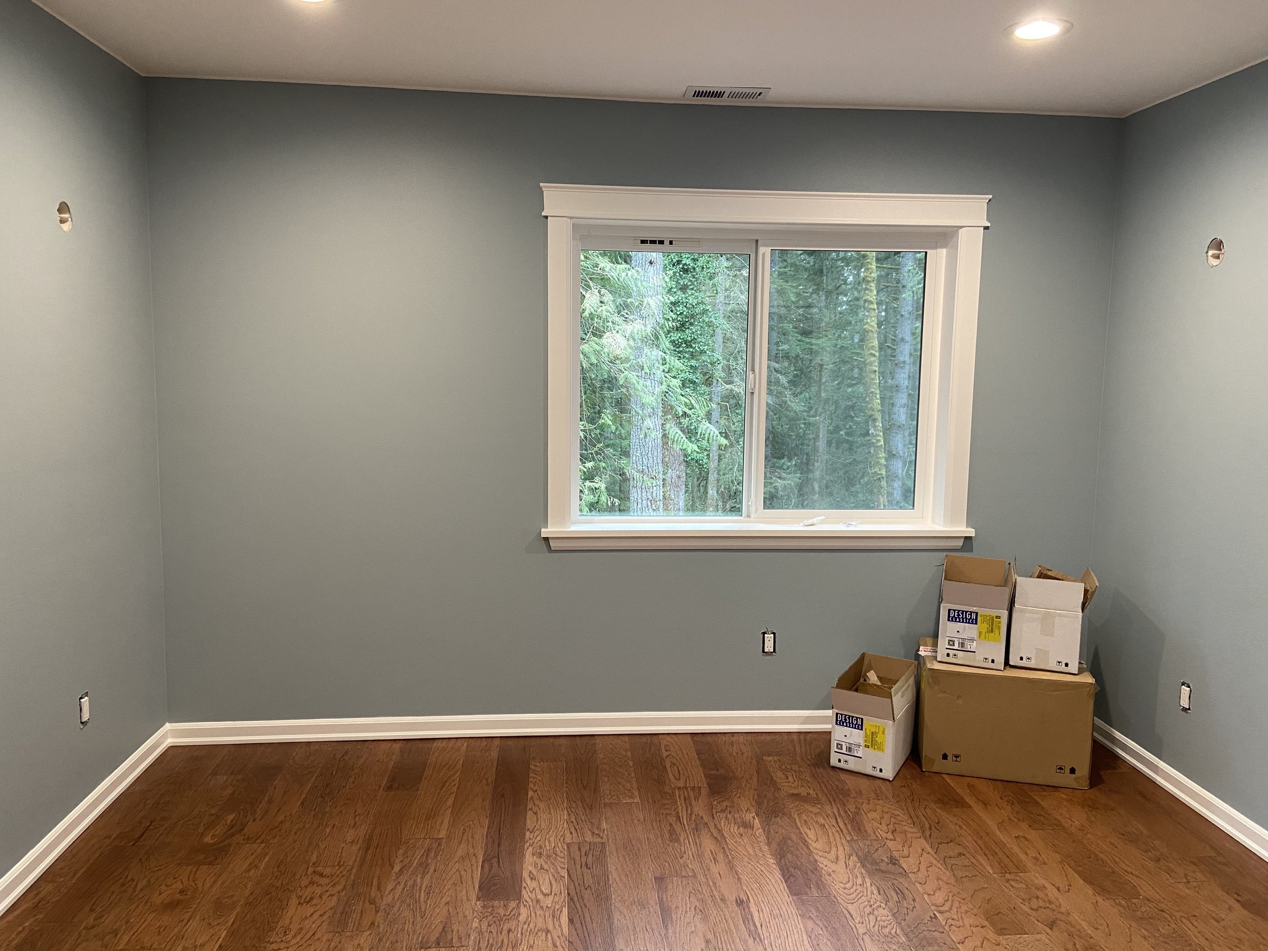 View of a large mountain range over a body of water with trees in the foreground and a building on the right.