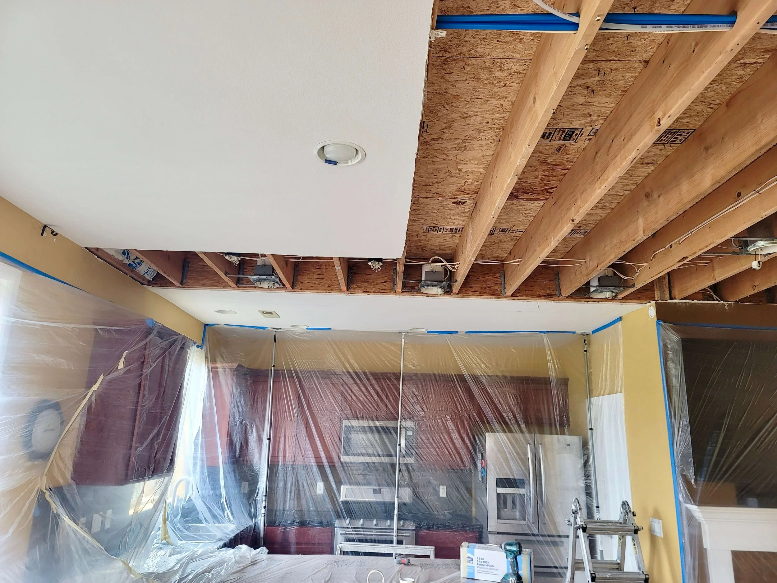 Before drywall installation in a Lynnwood WA home showing ceiling demolition with exposed framing, electrical, and containment setup prior to finishing.