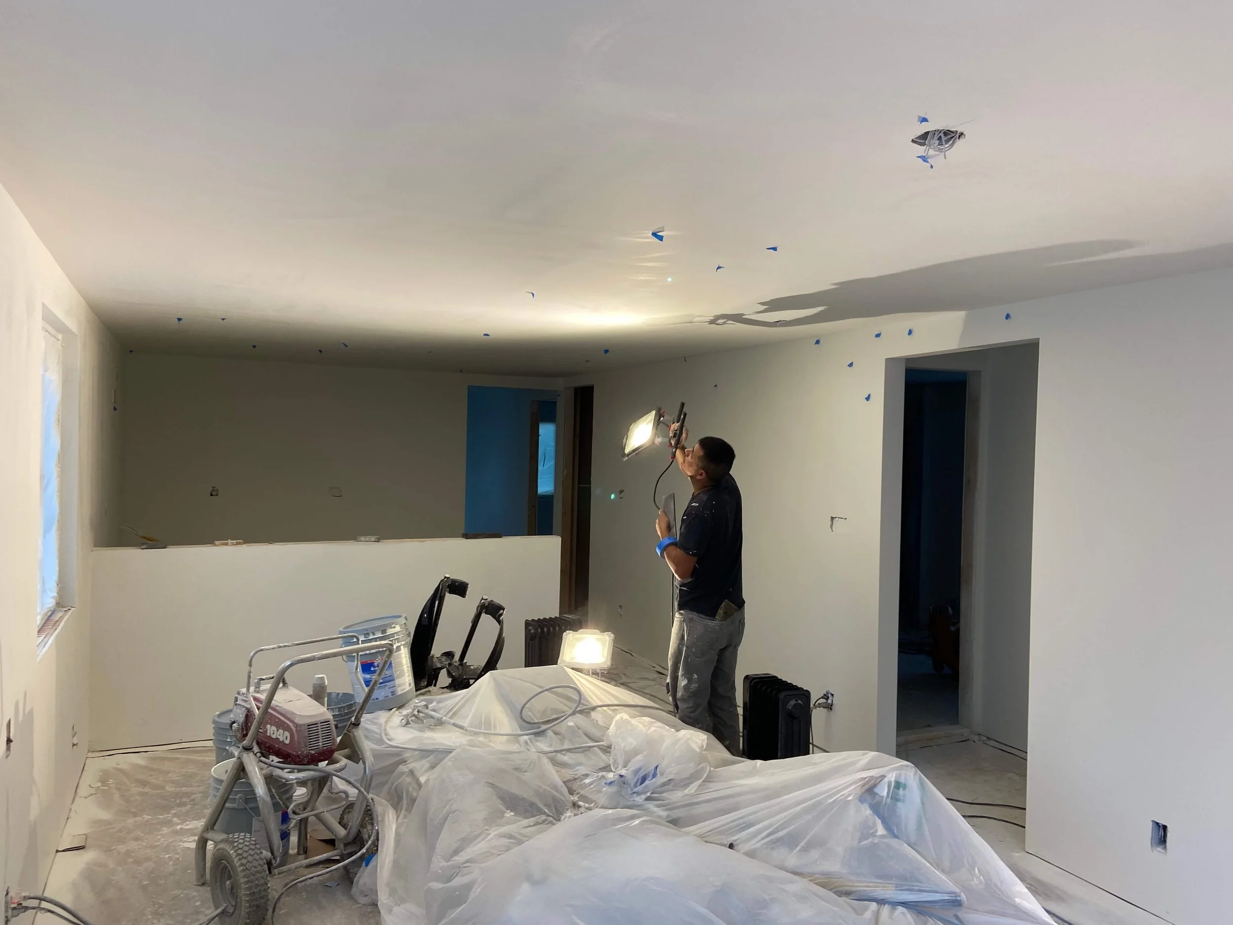 Drywall finisher inspecting a North Seattle ceiling with a work light, with blue tape marking areas for touch-ups.