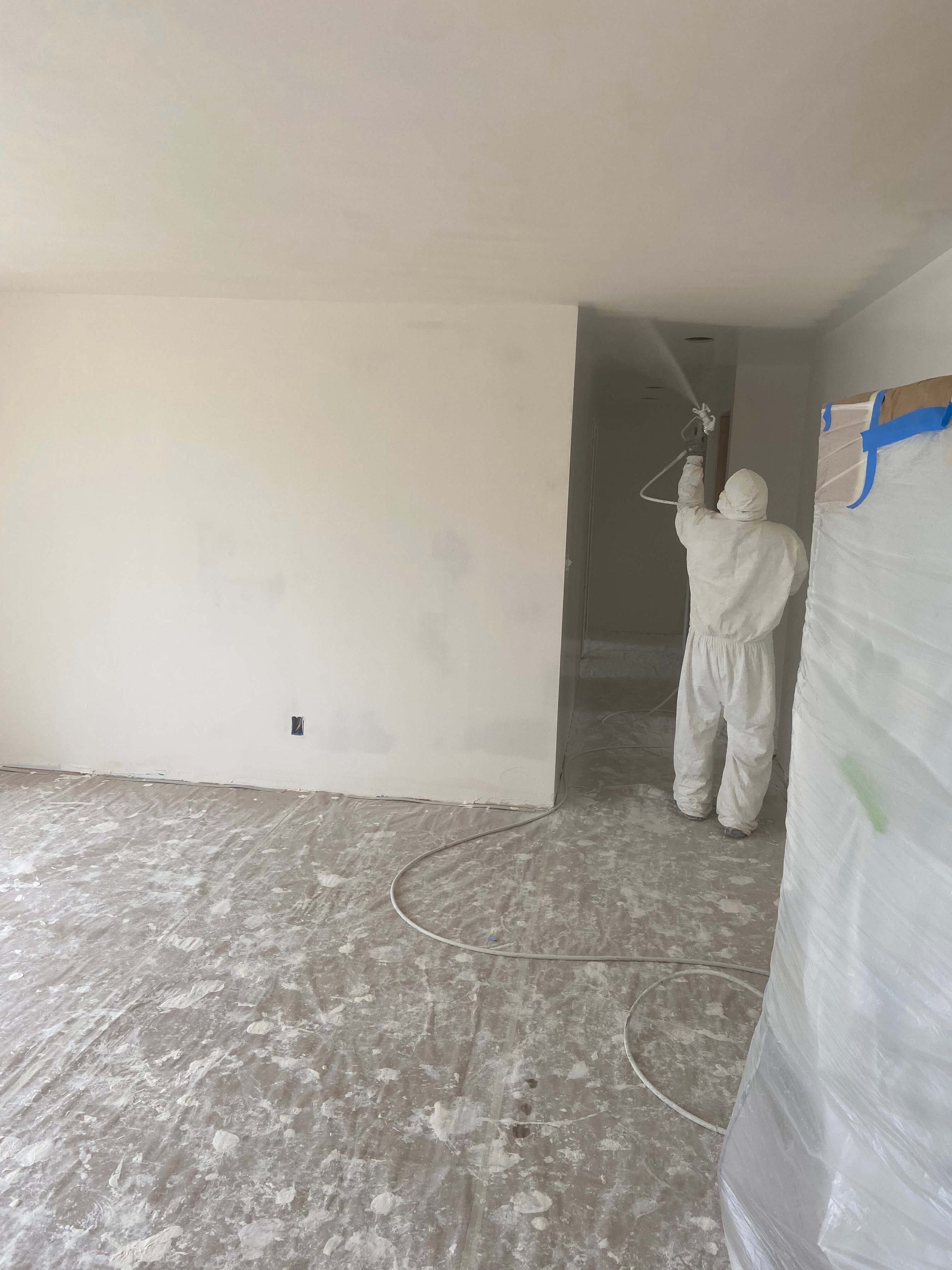Worker spraying PVA primer onto drywall in a Redmond project, with nearby surfaces masked and floors protected.