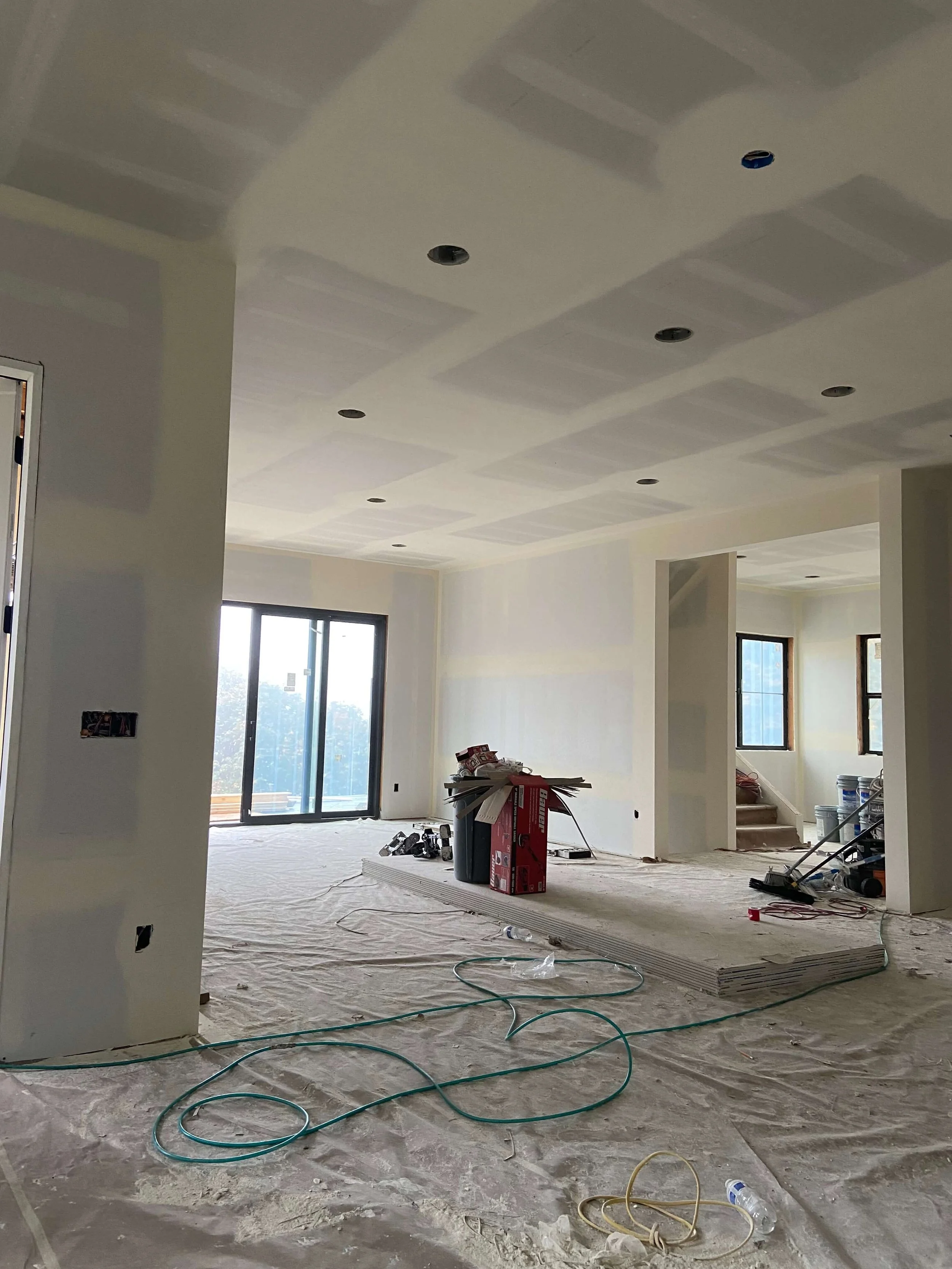Snohomish custom home during drywall finishing with taped ceiling joints, open rooms, large windows, and construction equipment.