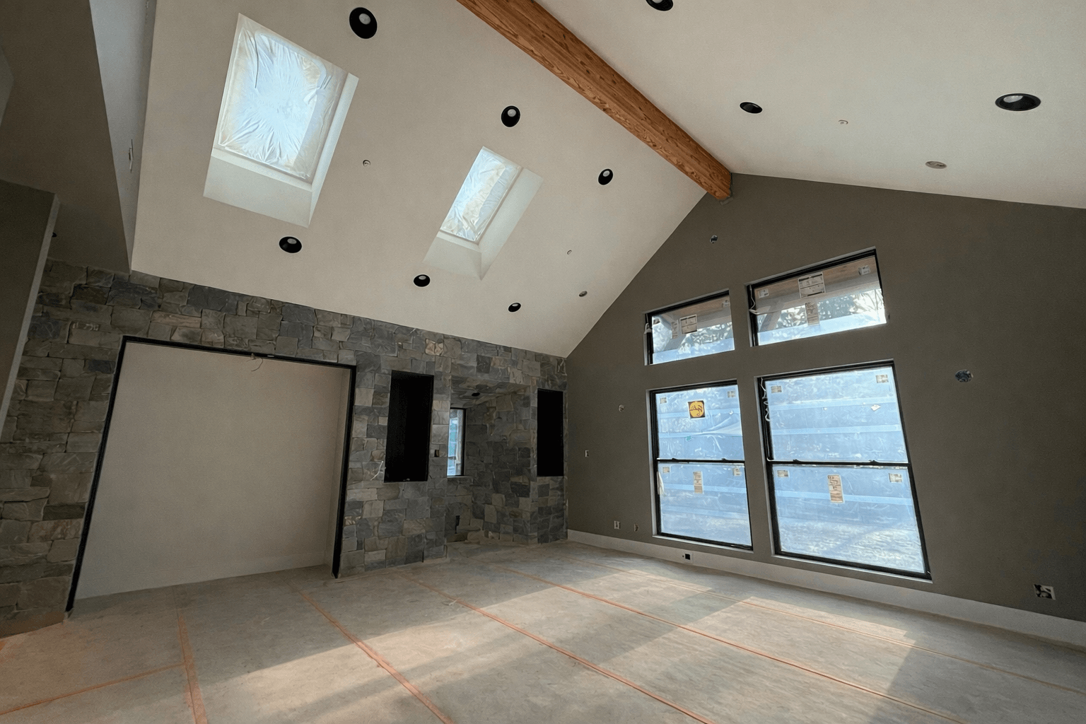 Duvall living room after drywall finishing and painting, with a vaulted ceiling, exposed wood beam, stone fireplace, and protected flooring.