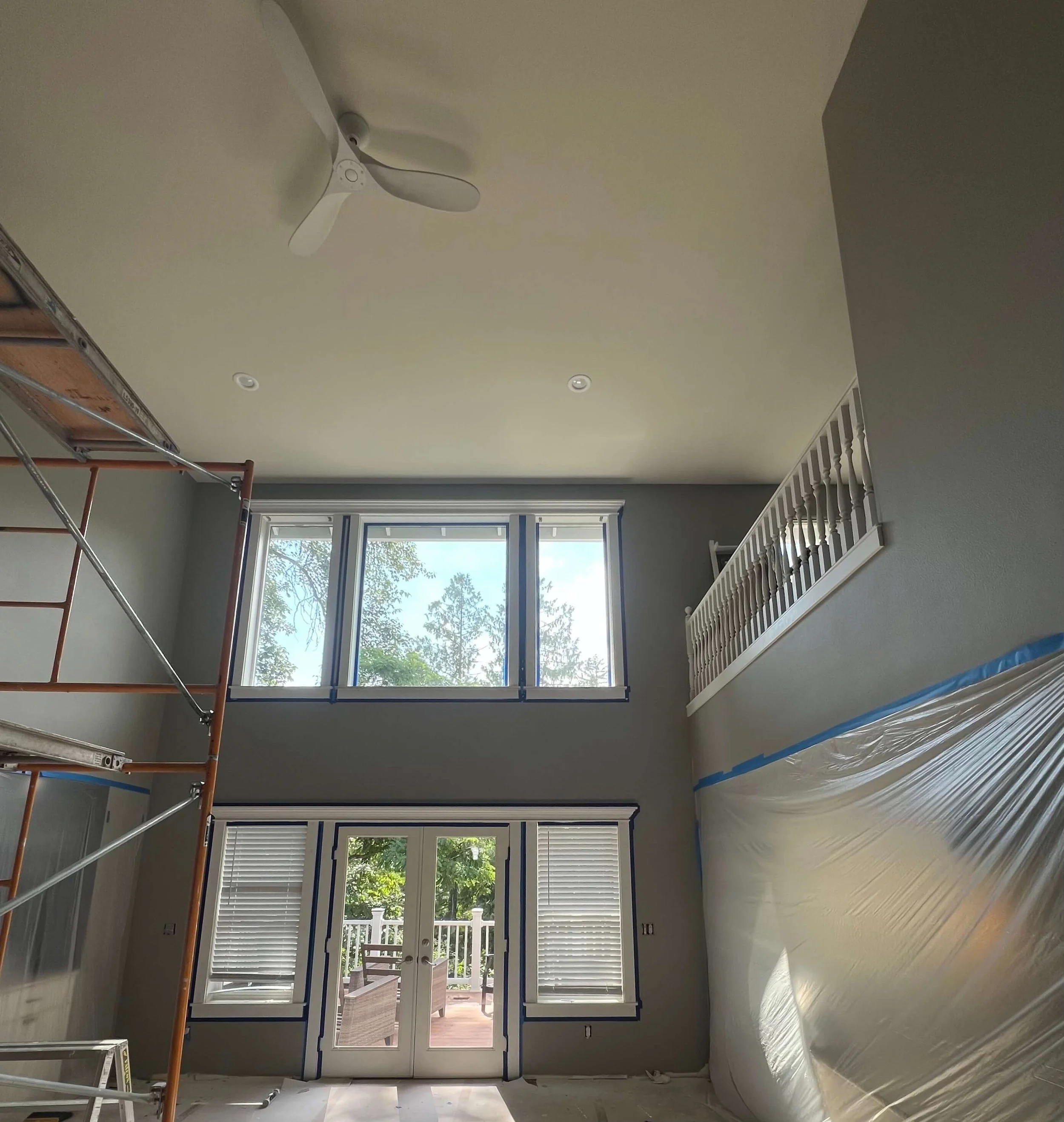 Duvall two-story room after wall and ceiling drywall restoration, with a finished ceiling, gray walls, white window and door trim, and scaffolding still in place.
