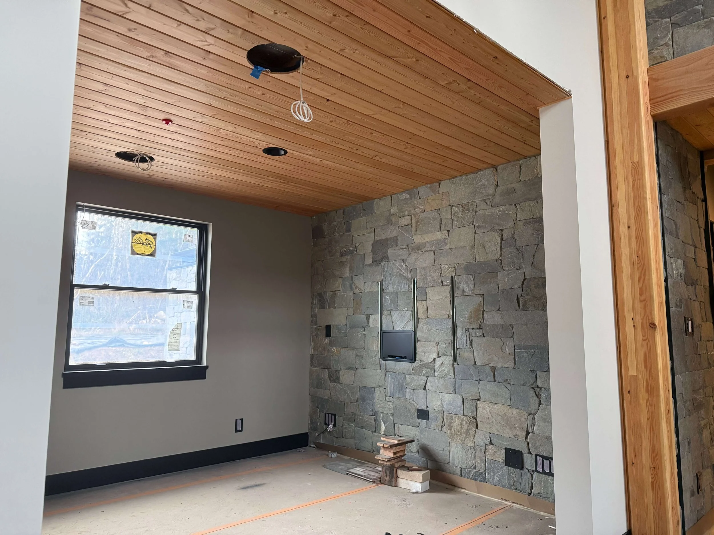 Duvall new custom home during final drywall finishing, primer, and spray painting with a vaulted wood ceiling and stone accent wall