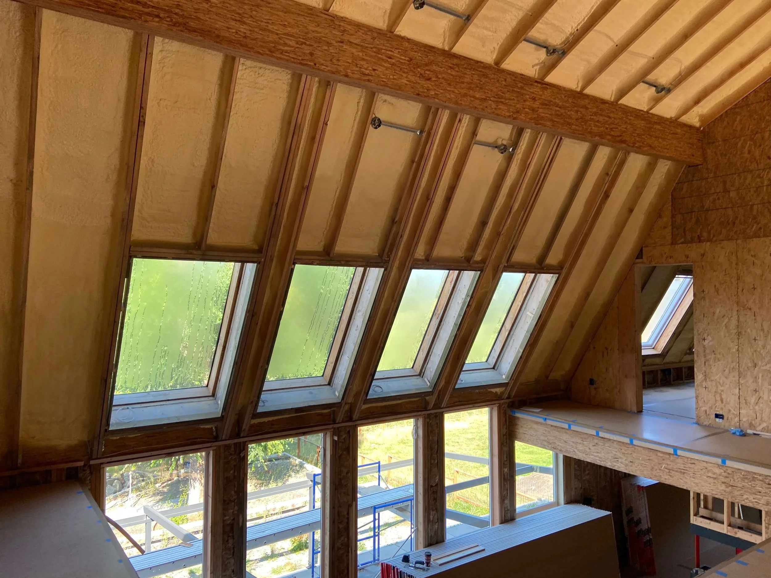 Redmond loft before drywall installation, with exposed framing, roof insulation, a wood beam, angled windows, and protected walkways.