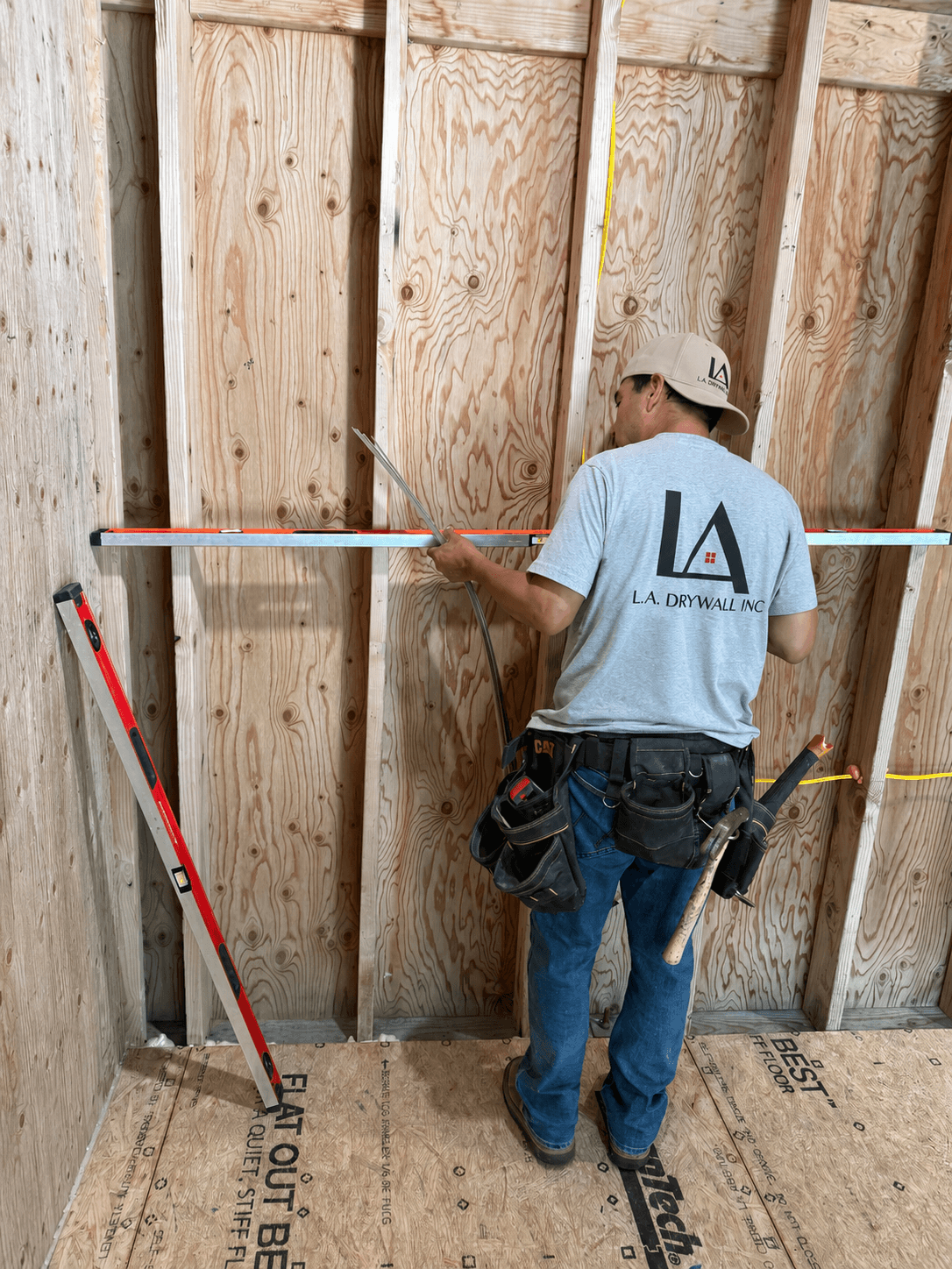 L.A. Drywall crew member checking wood framing with a level during pre-drywall preparation at a residential project in Kenmore, Washington.