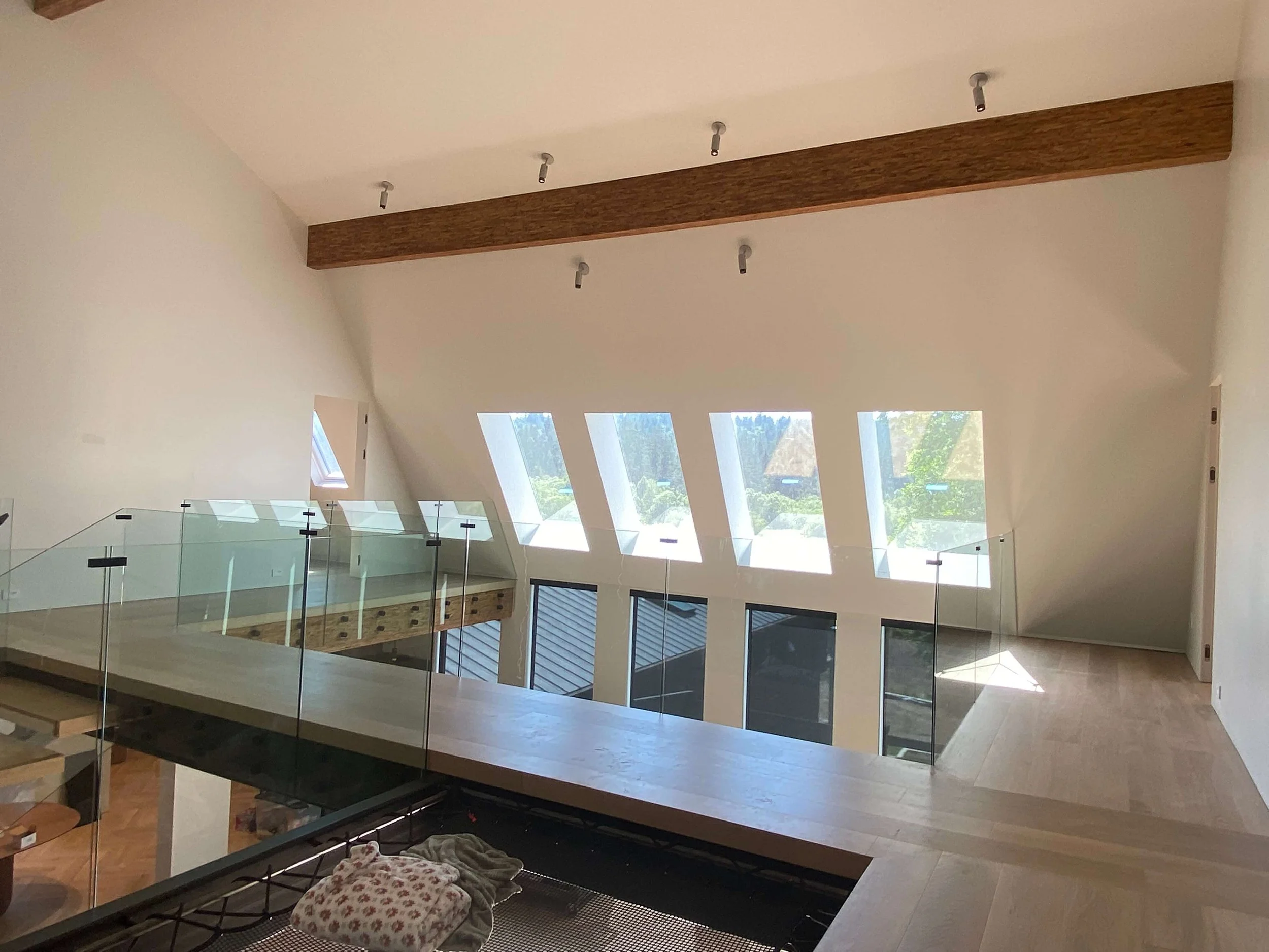 Finished drywall walls and angled window returns around a loft with glass railings and exposed wood beams in Redmond, WA.