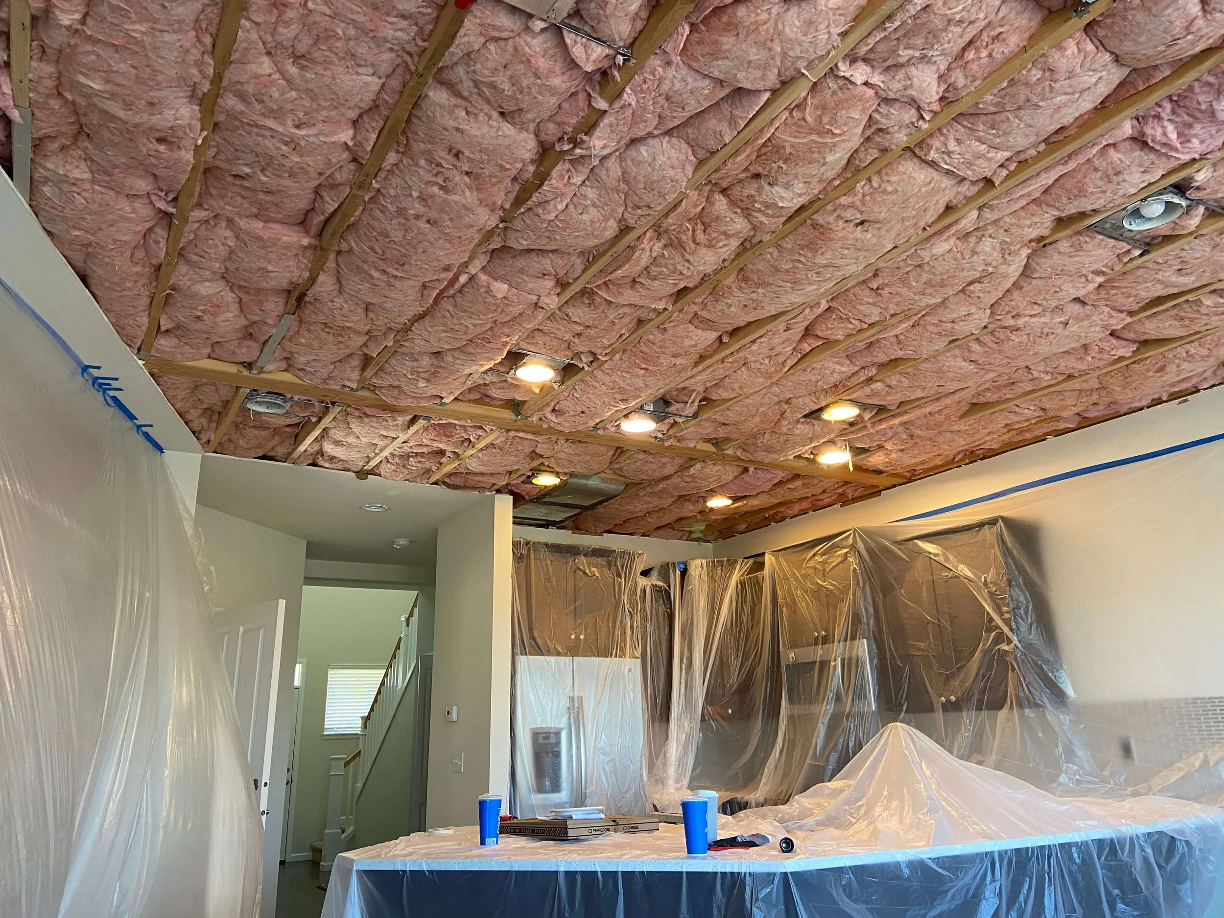 Insulated ceiling framing and plastic-covered kitchen cabinets before drywall replacement in Lynnwood, WA.