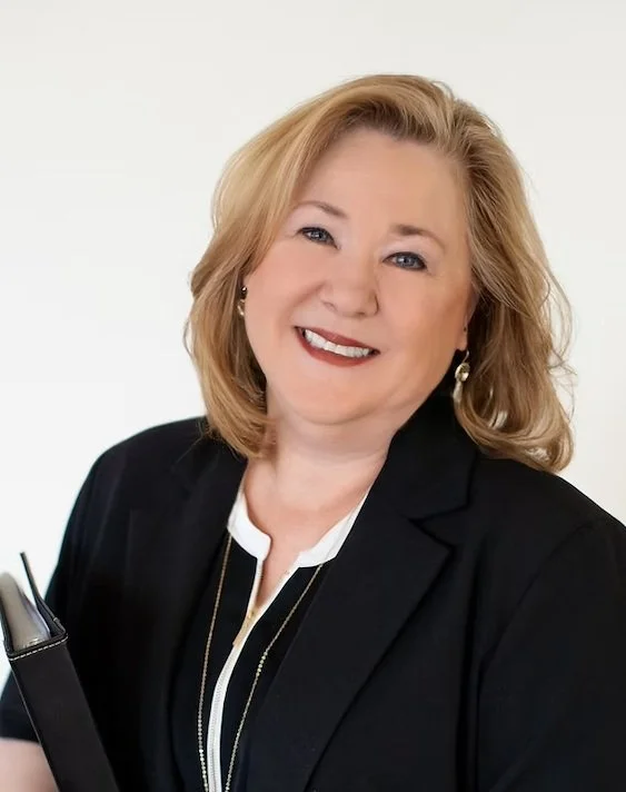 A smiling woman with blonde hair in business attire, posing against a plain white background.