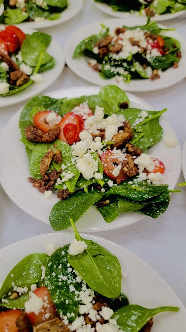 Salads with spinach, sliced strawberries, crumbled cheese, and nuts on white plates.