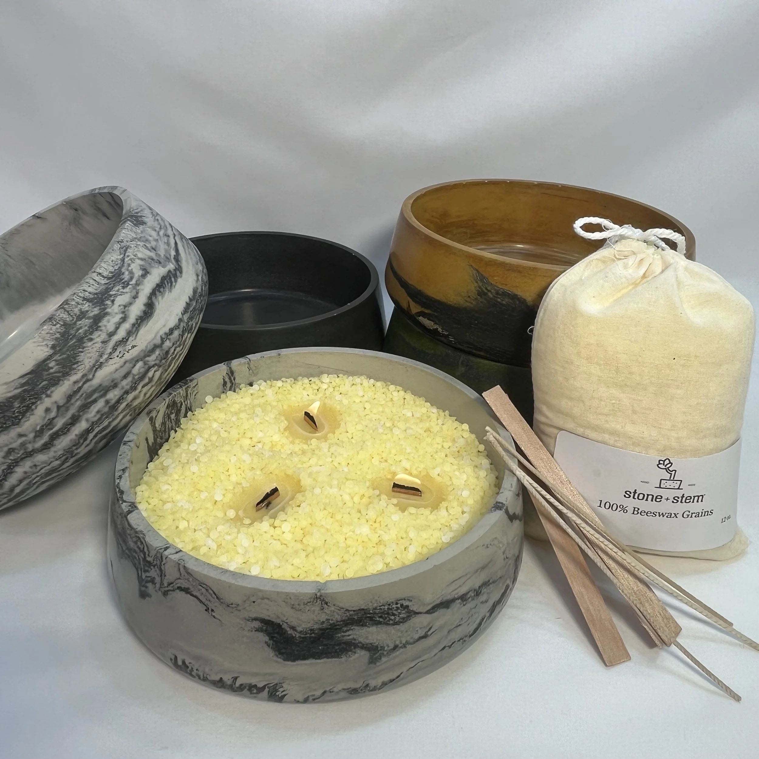 collection of concrete dishes with a bag of beeswax grains, three cotton wicks and three wooden wicks