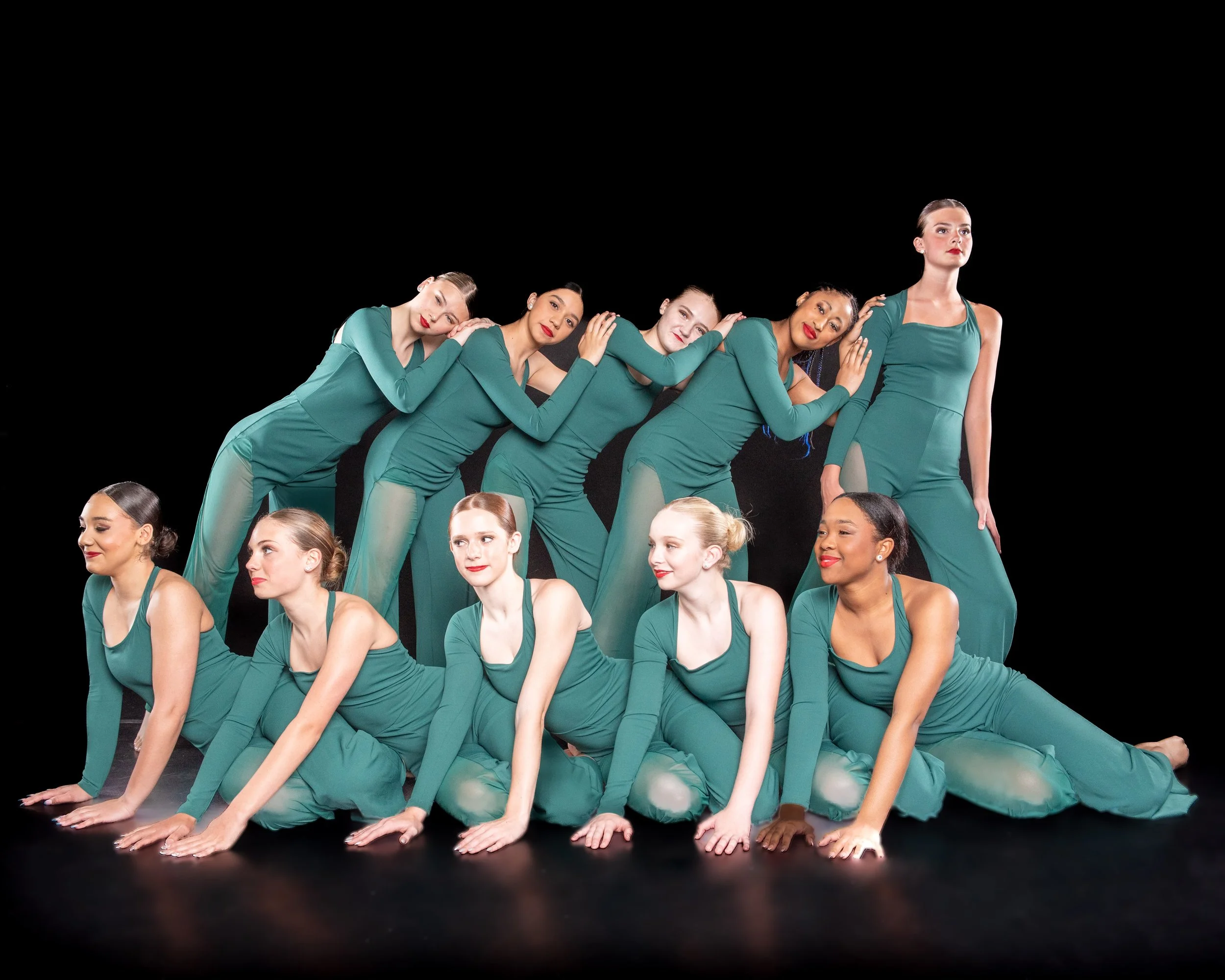 Group of diverse women in matching teal outfits performing a coordinated yoga pose on a black background.