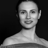 Black and white portrait of a young woman with dark hair, wearing an off-the-shoulder top and a necklace, smiling gently at the camera.
