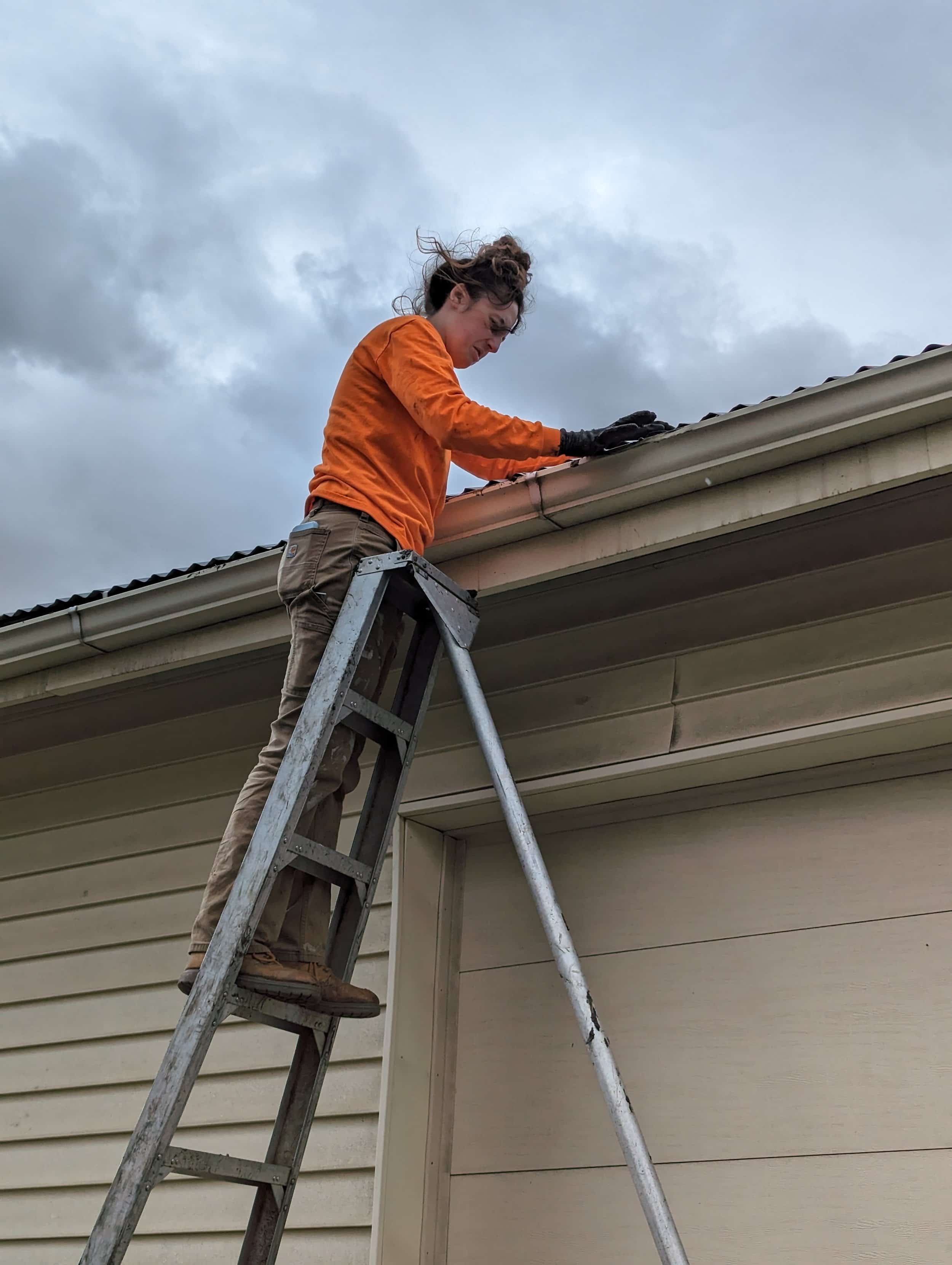 woman cleaning gutters on ladder